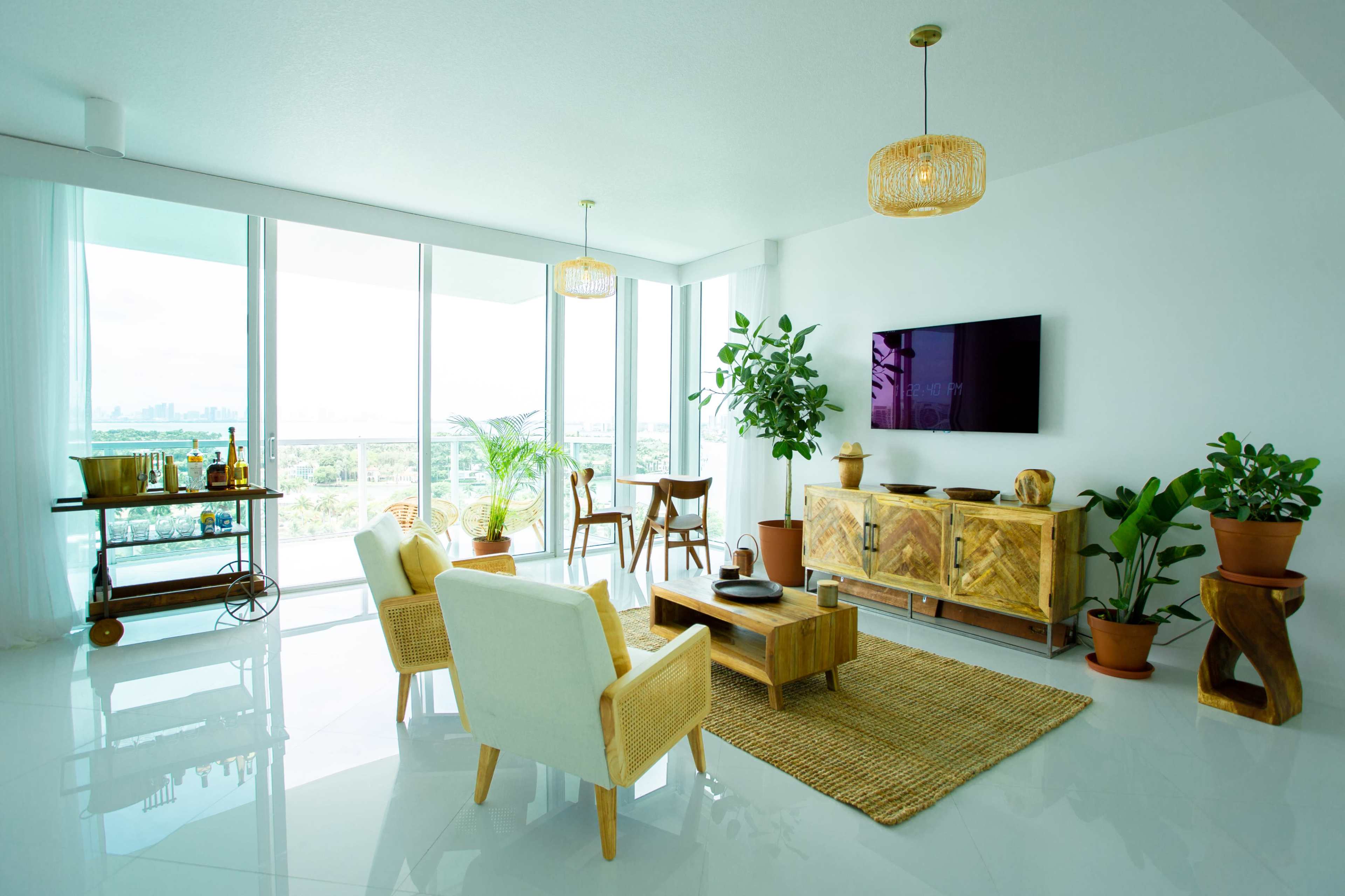 A bright living room features large windows with city views, minimalist furniture, and potted plants.
