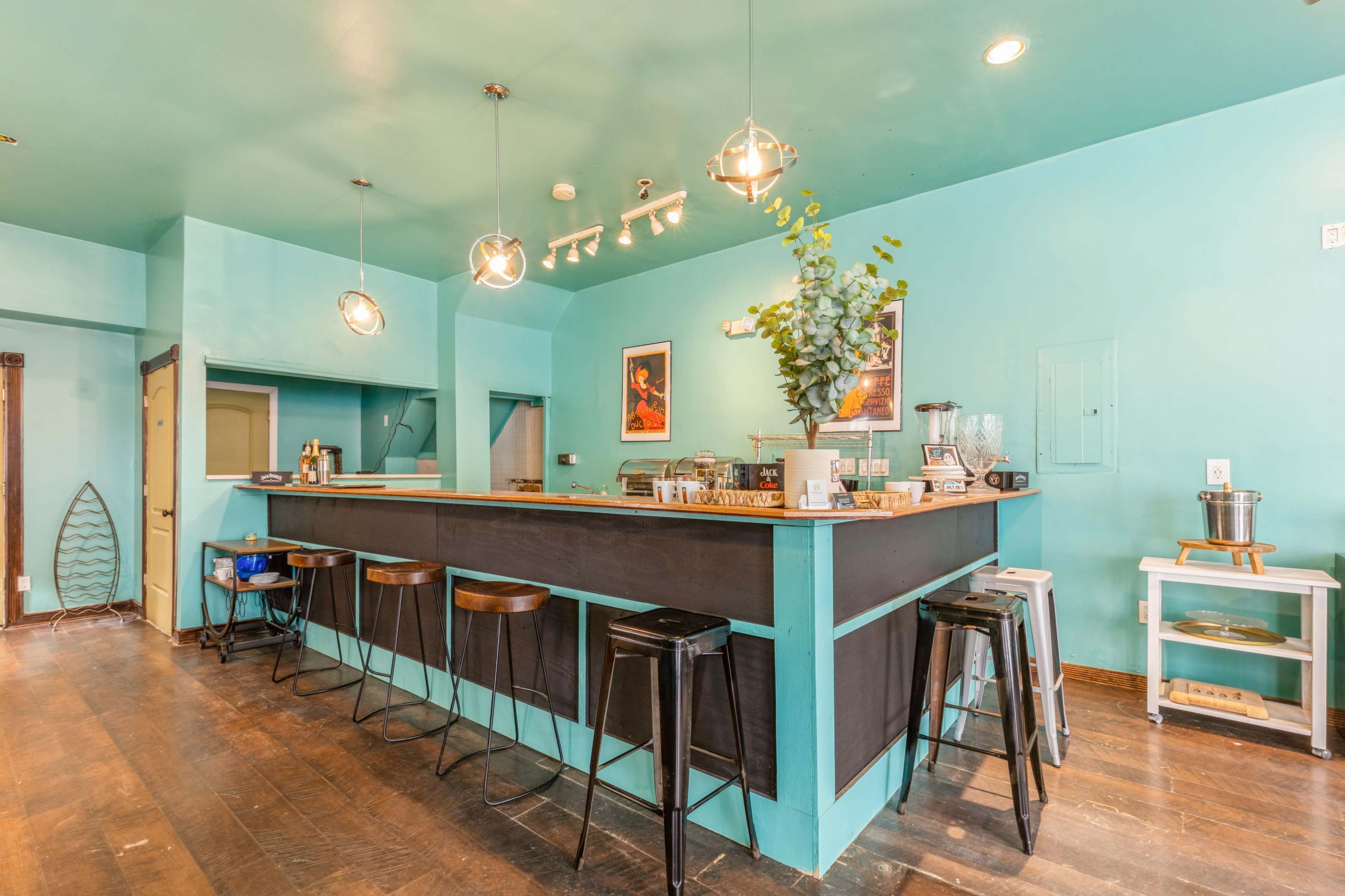A modern café interior features a turquoise-painted wall, a wooden bar with stools, and decorative elements.