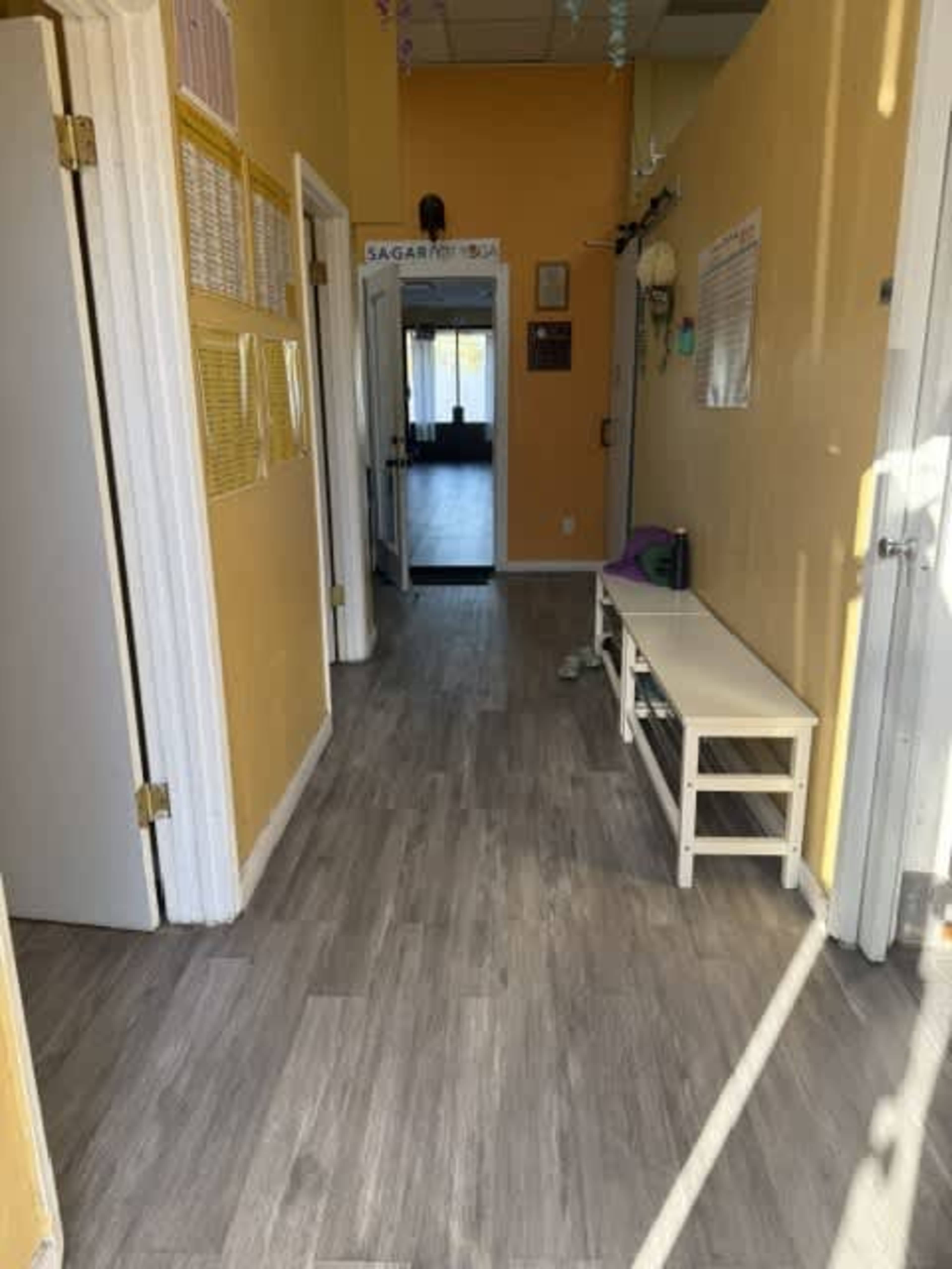 A brightly lit hallway with yellow walls features two doors on either side and a white bench against one wall.