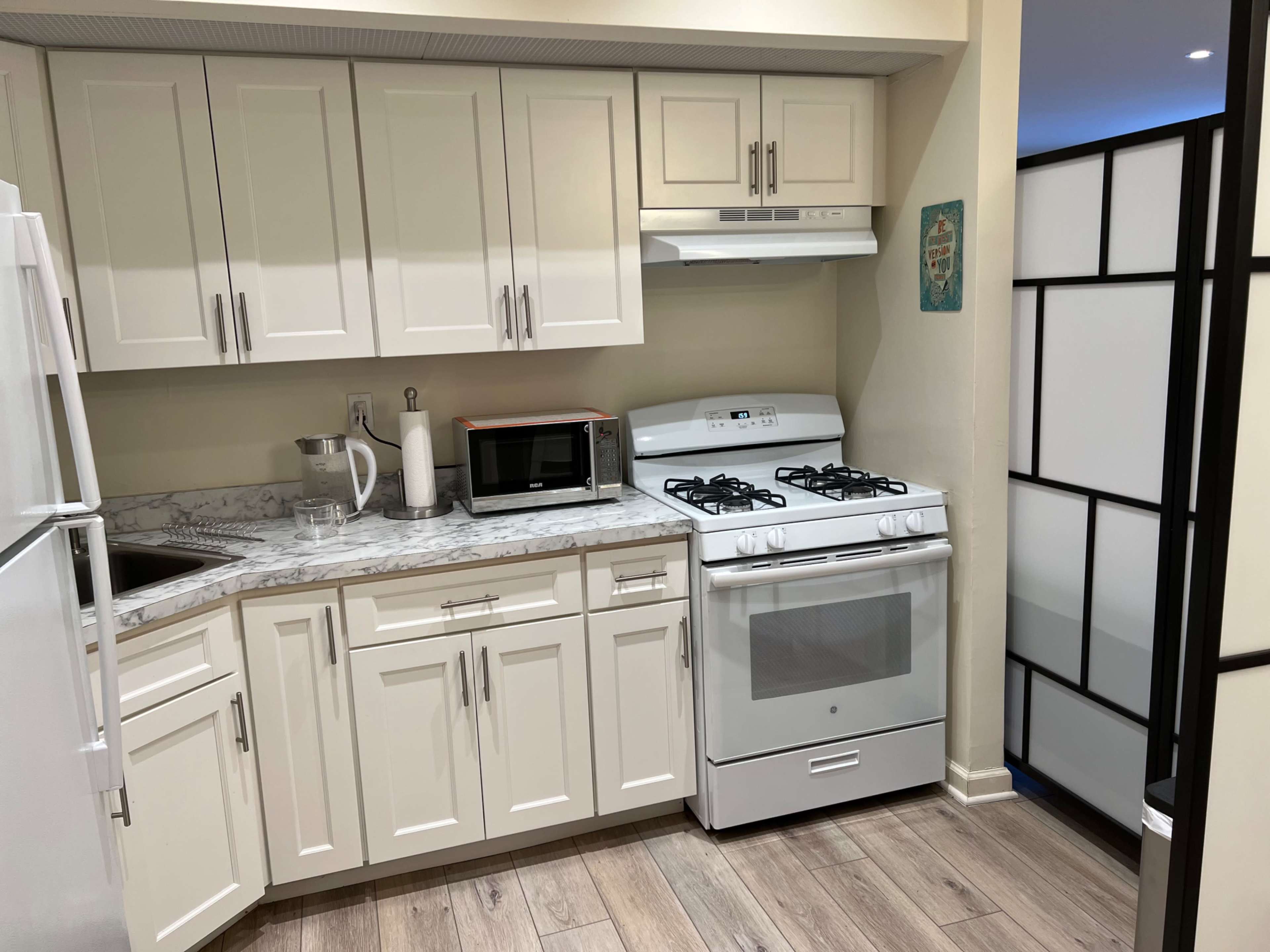 A compact kitchen features white cabinetry, a marble countertop, a gas stove, a refrigerator, and a microwave.