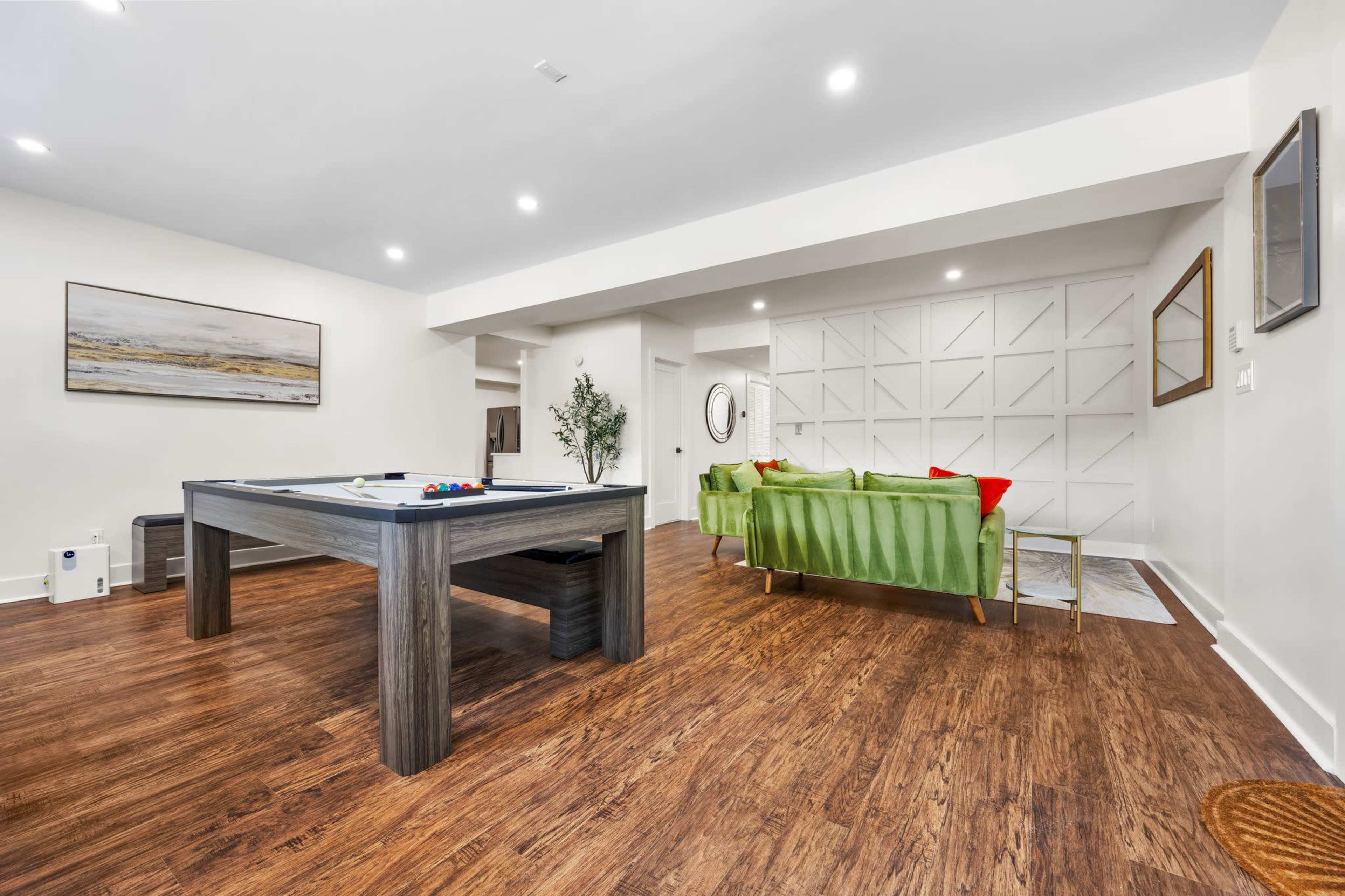 The image shows a spacious living area featuring a billiards table, a green couch, and wooden flooring.