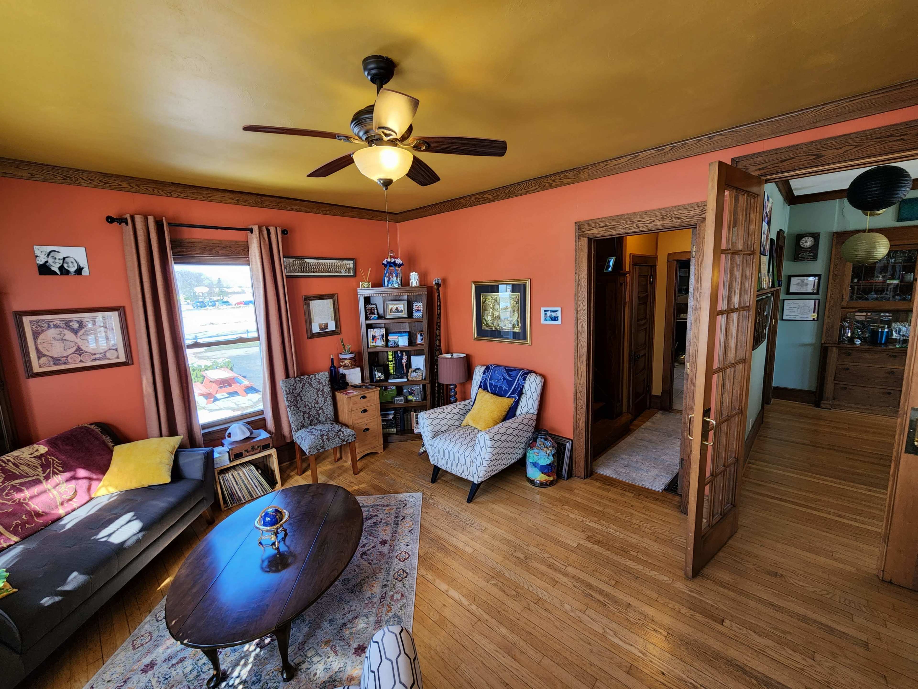 A cozy living room with a patterned rug, a wooden coffee table, a sofa, and two chairs, all against a vividly painted orange wall.