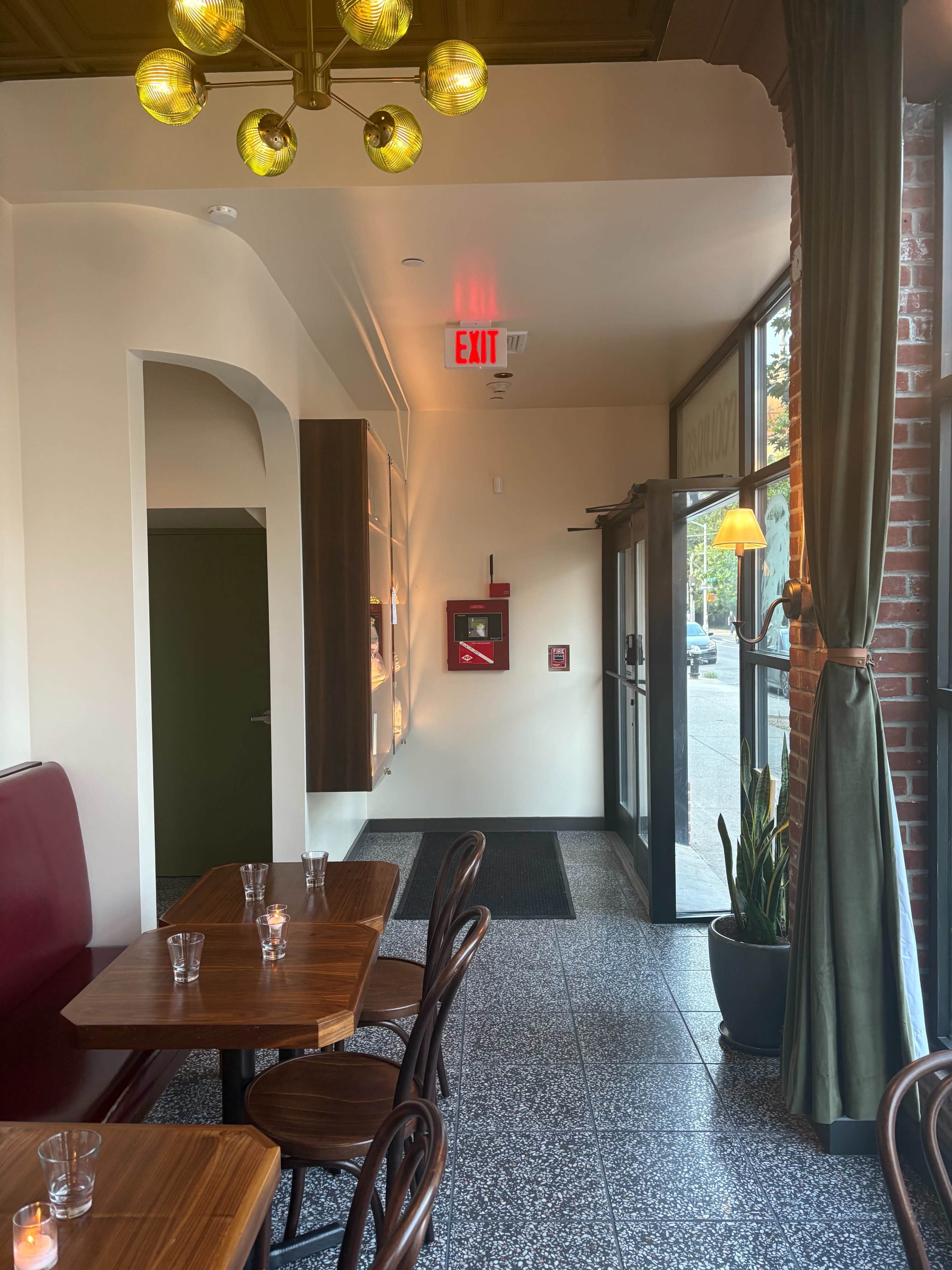 The image shows a café interior with wooden tables, green curtains, and a bright exit sign near the entrance.