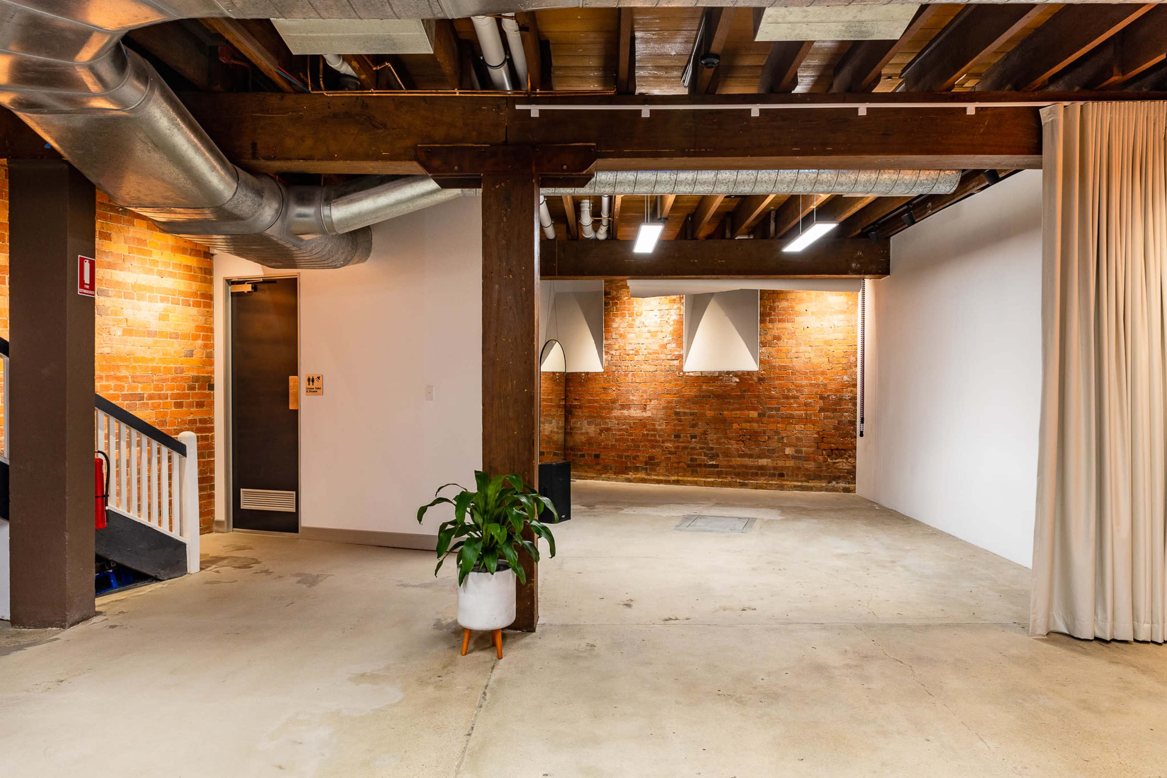 A spacious industrial-style interior with exposed brick walls, concrete flooring, and a plant in a white pot, featuring an exit door and soft lighting.