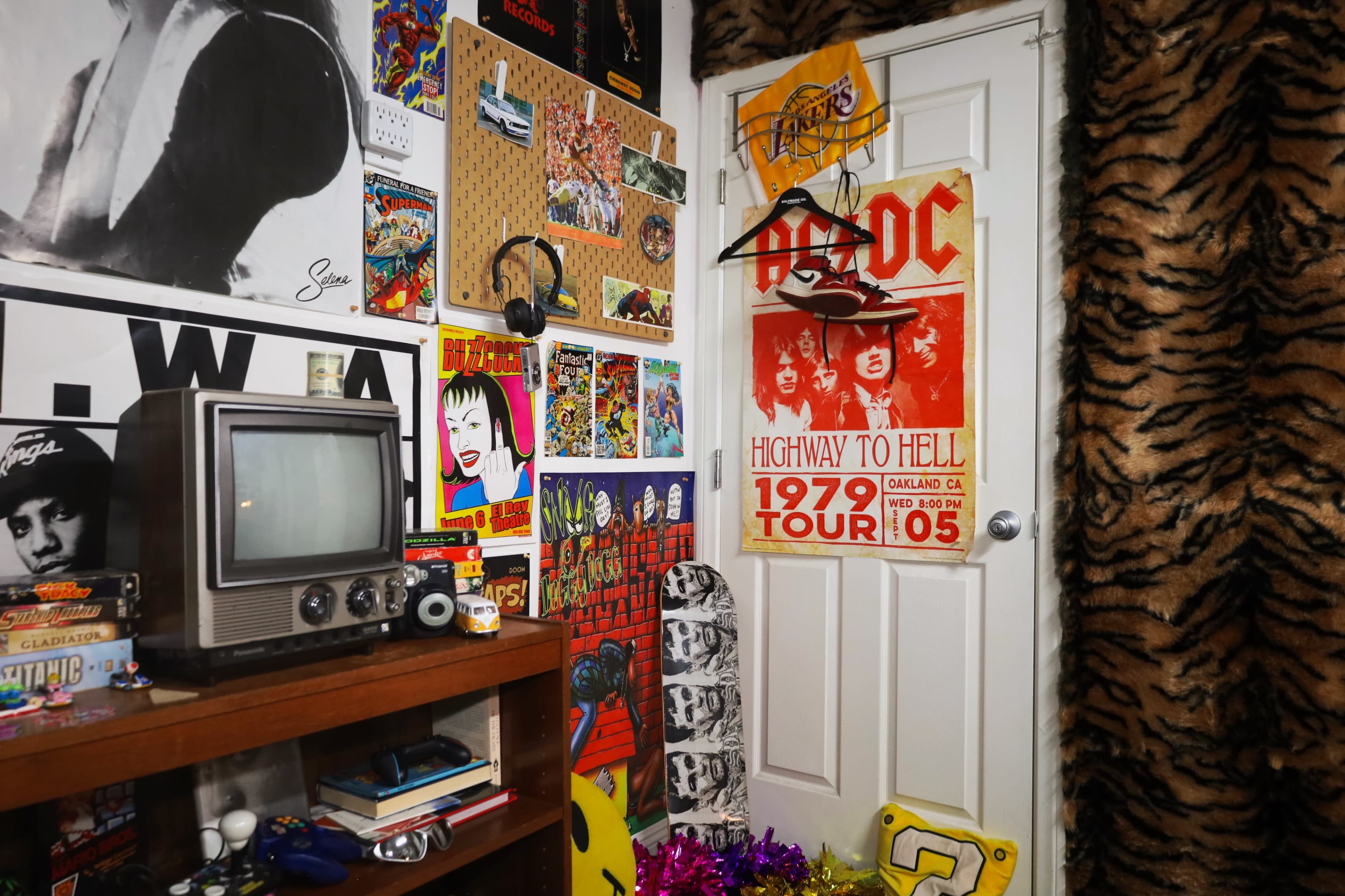 The image shows a cluttered room featuring a vintage television, colorful posters on the walls, and various memorabilia scattered throughout the space.