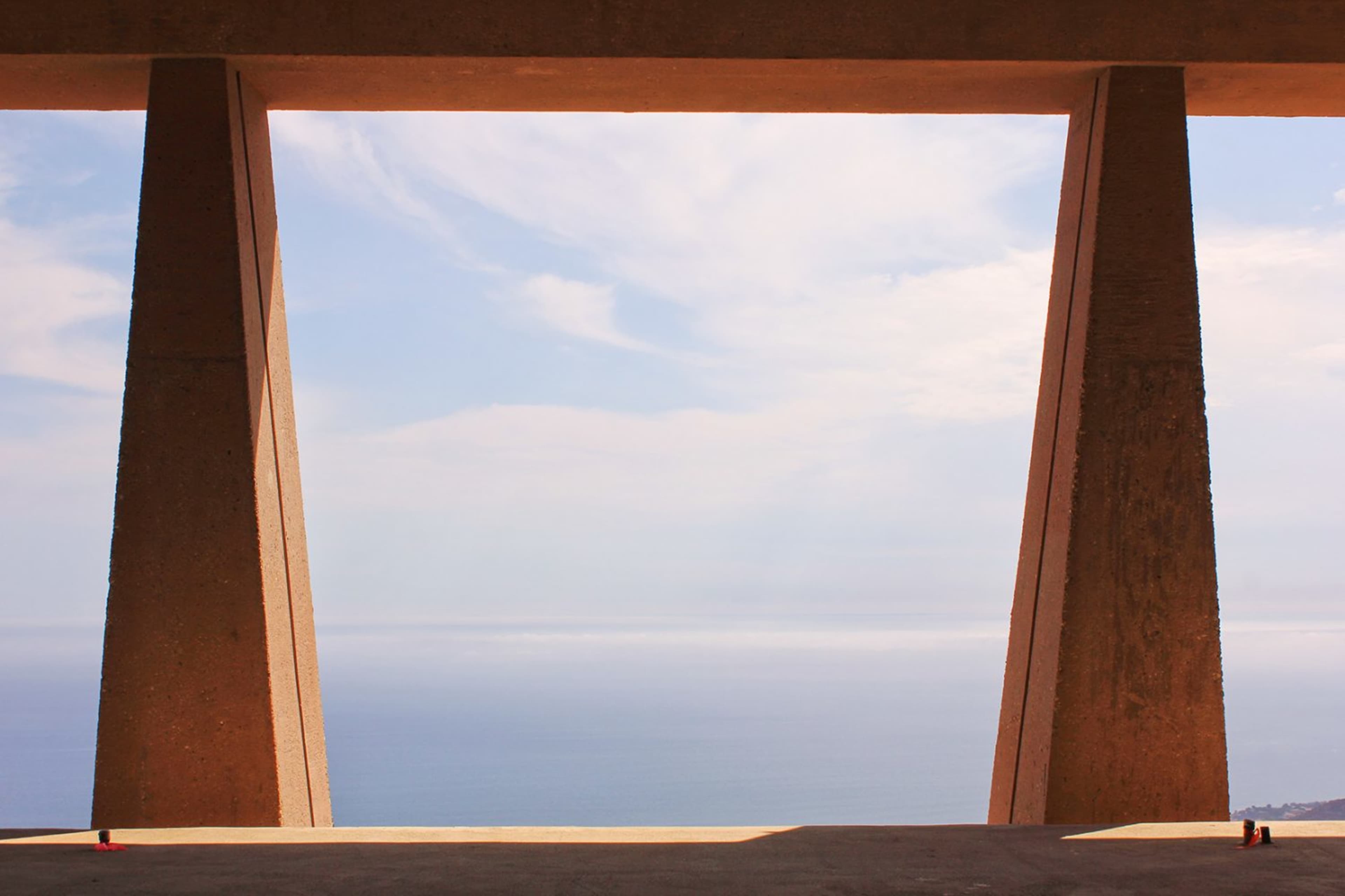 The image shows a concrete structure with two large pillars framing a view of the ocean and sky.