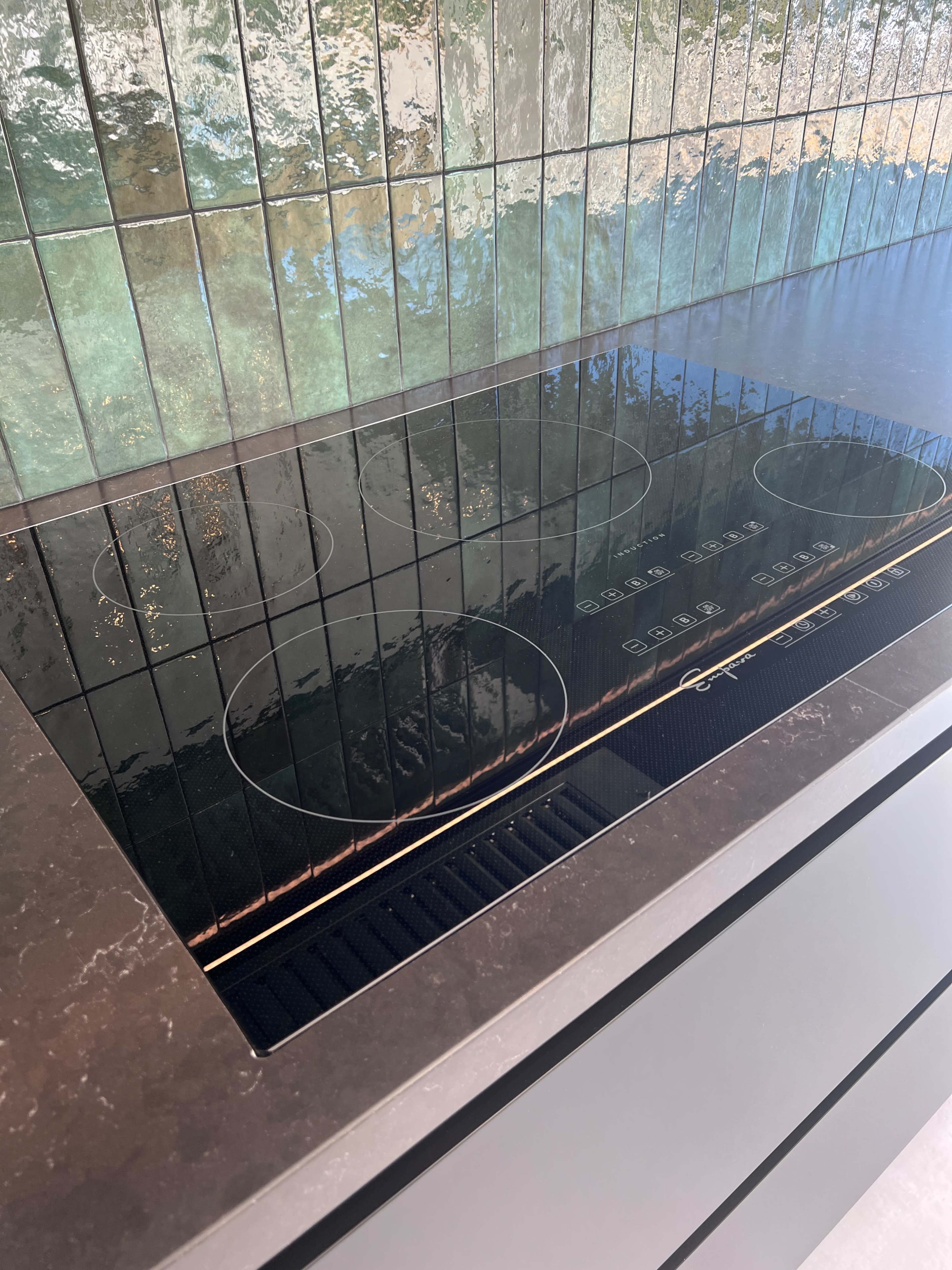 The image shows a sleek black induction cooktop embedded in a countertop with a reflective tile backsplash.