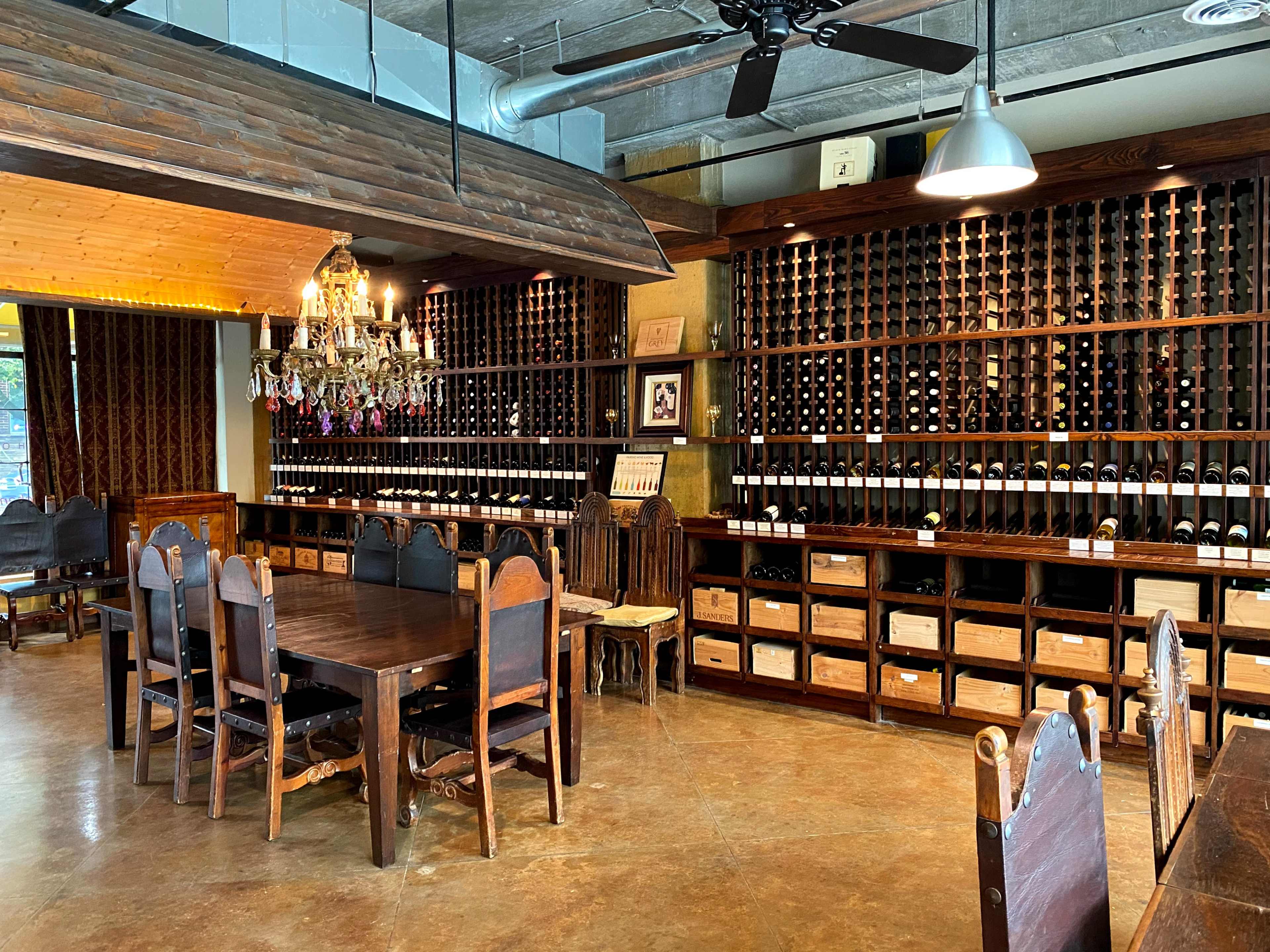 A wine-tasting room with wooden shelves filled with bottles of wine, a large wooden dining table, and a chandelier hanging from the ceiling.