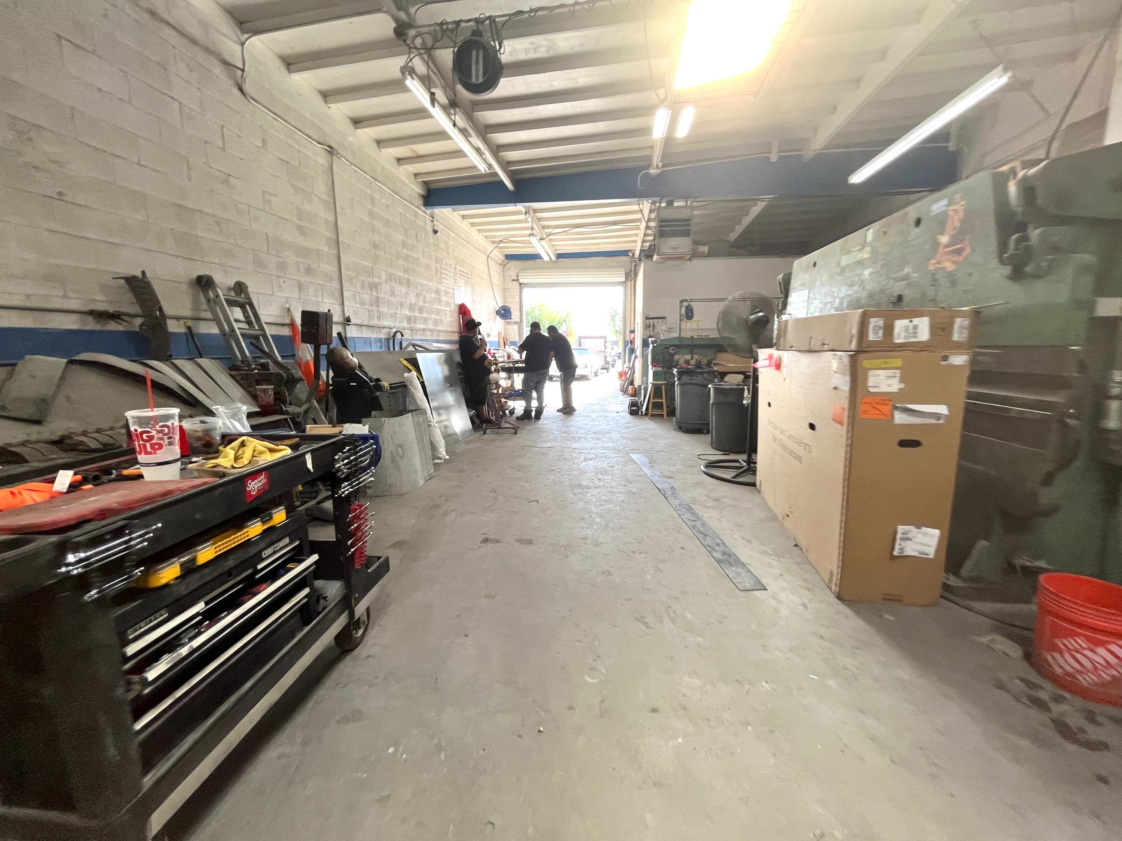 A narrow workshop hallway leads to an open area with various tools and equipment lining the walls.