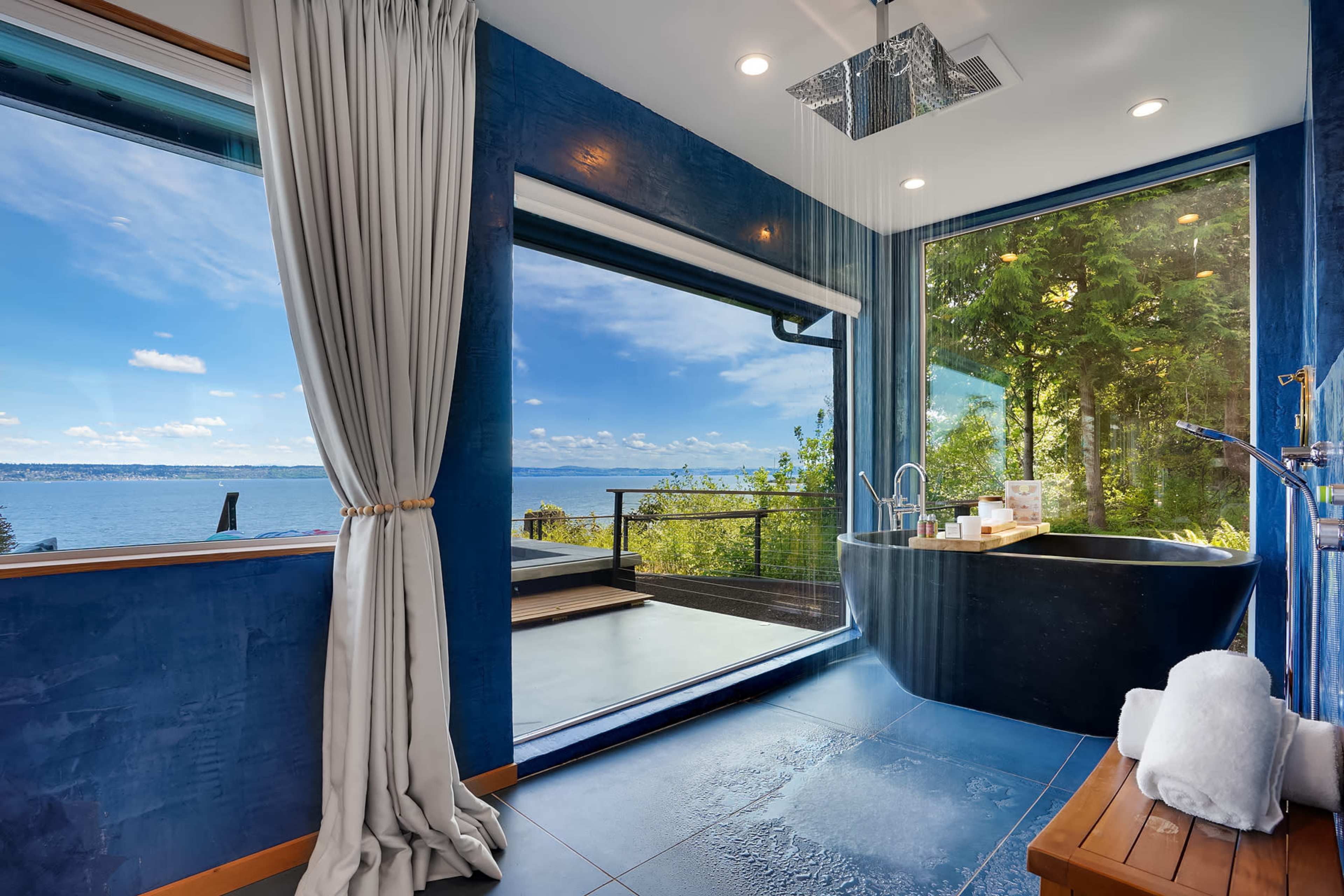 A modern bathroom featuring a large bathtub and floor-to-ceiling windows that provide a view of a water landscape and greenery.