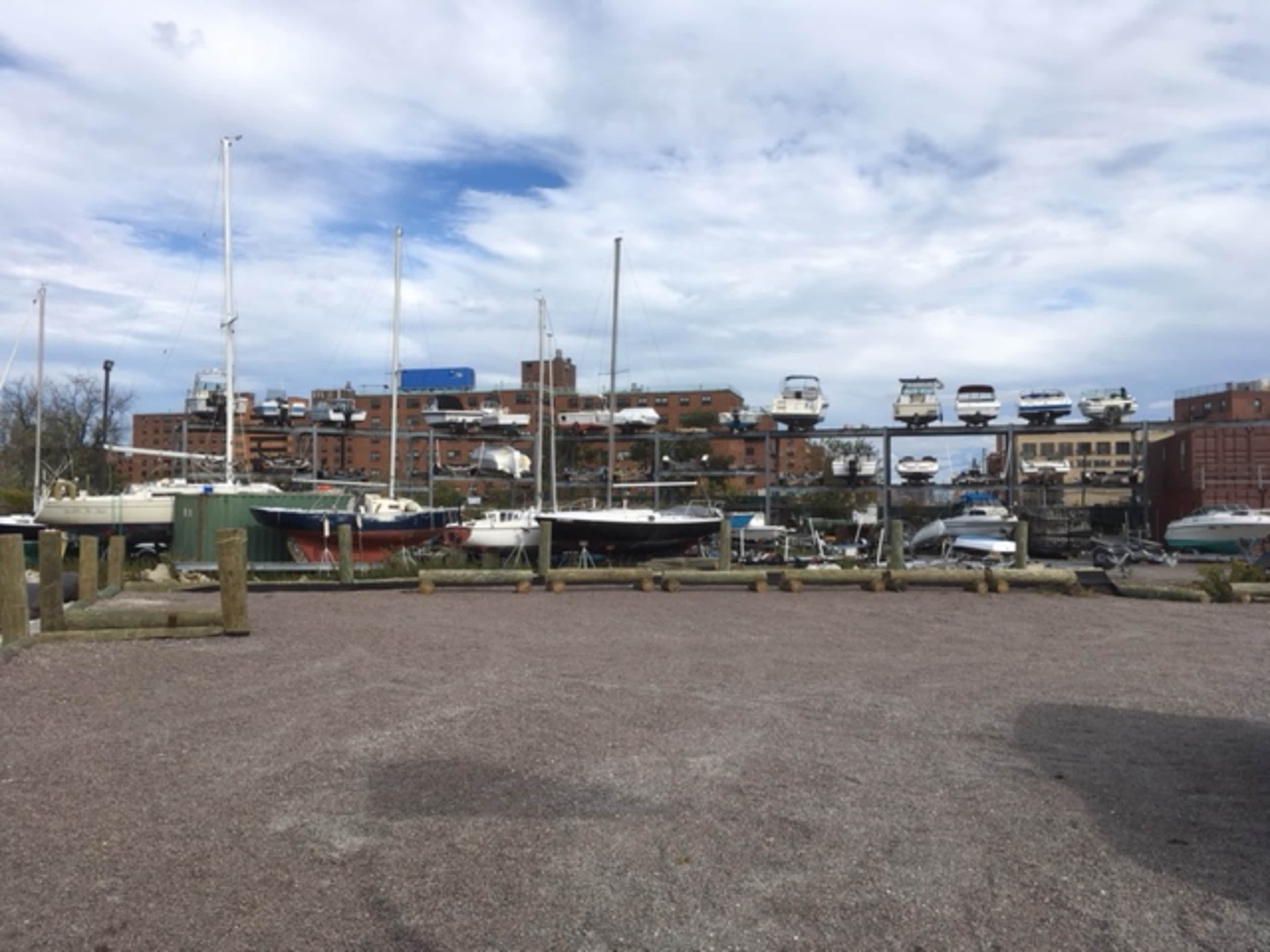 The scene shows a marina with several boats docked alongside buildings under a partly cloudy sky.
