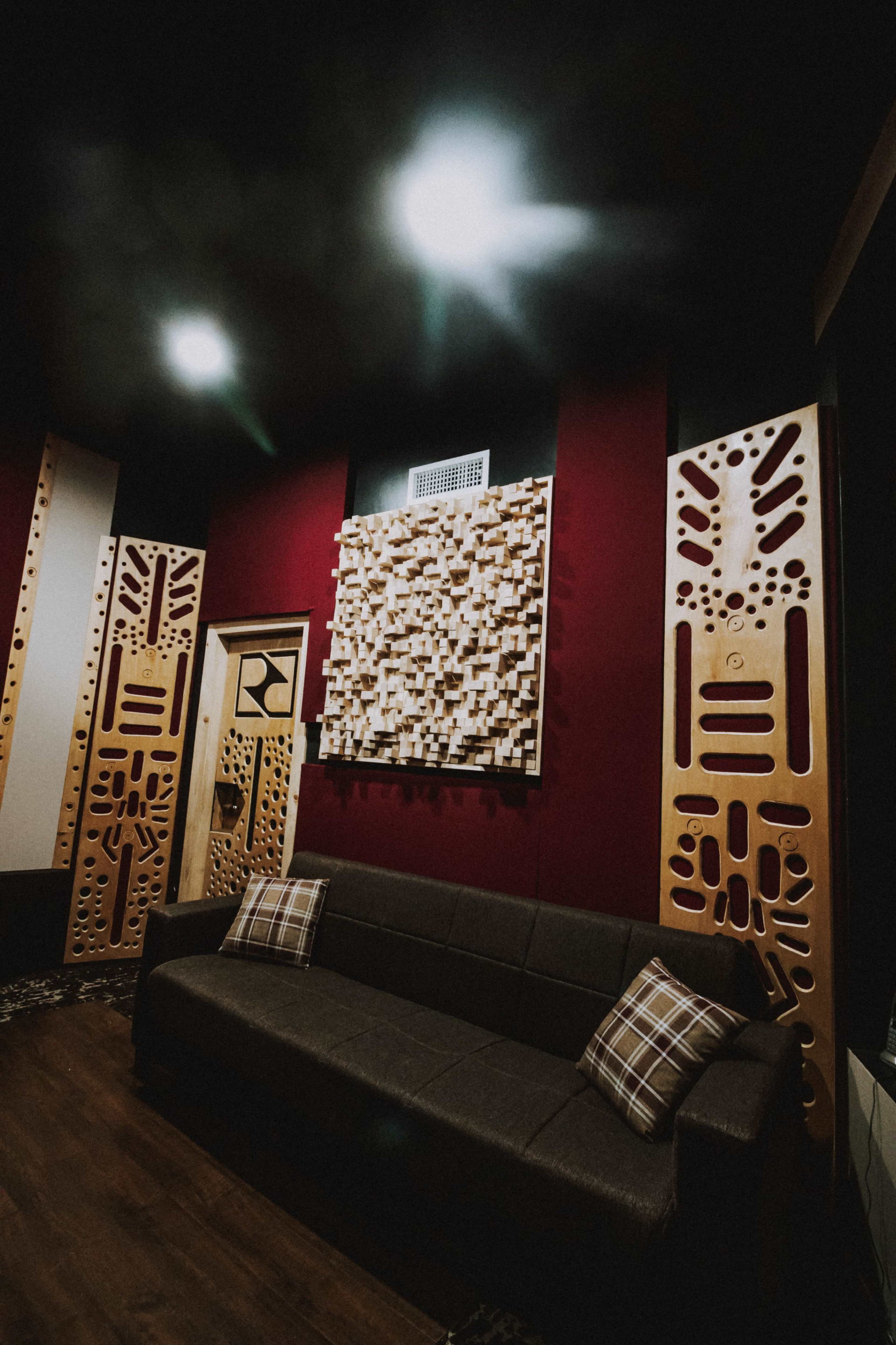 A small soundproof room featuring a dark gray sofa, decorative wall panels, and strategically placed lighting.