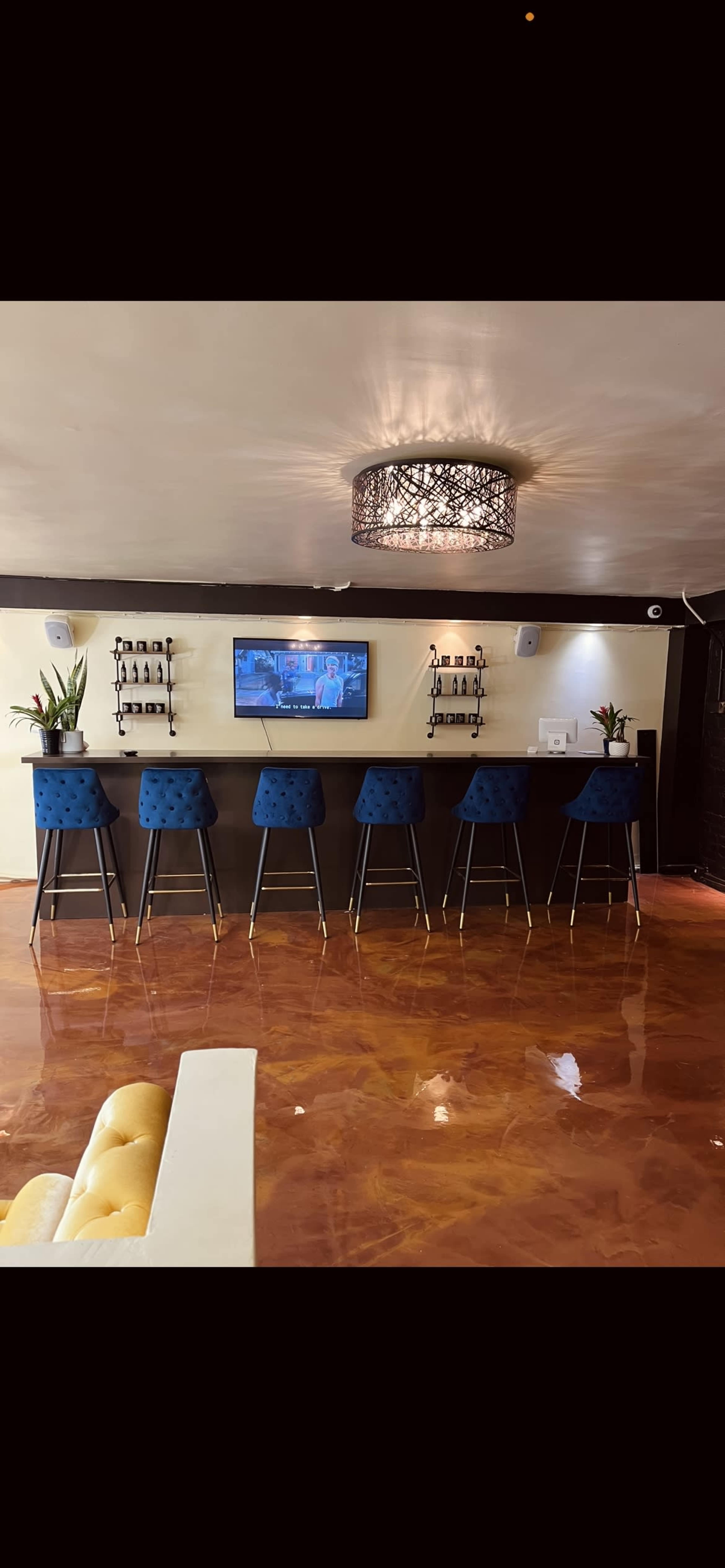 A modern bar area with blue stools, a television mounted on the wall, and a polished, reflective floor.