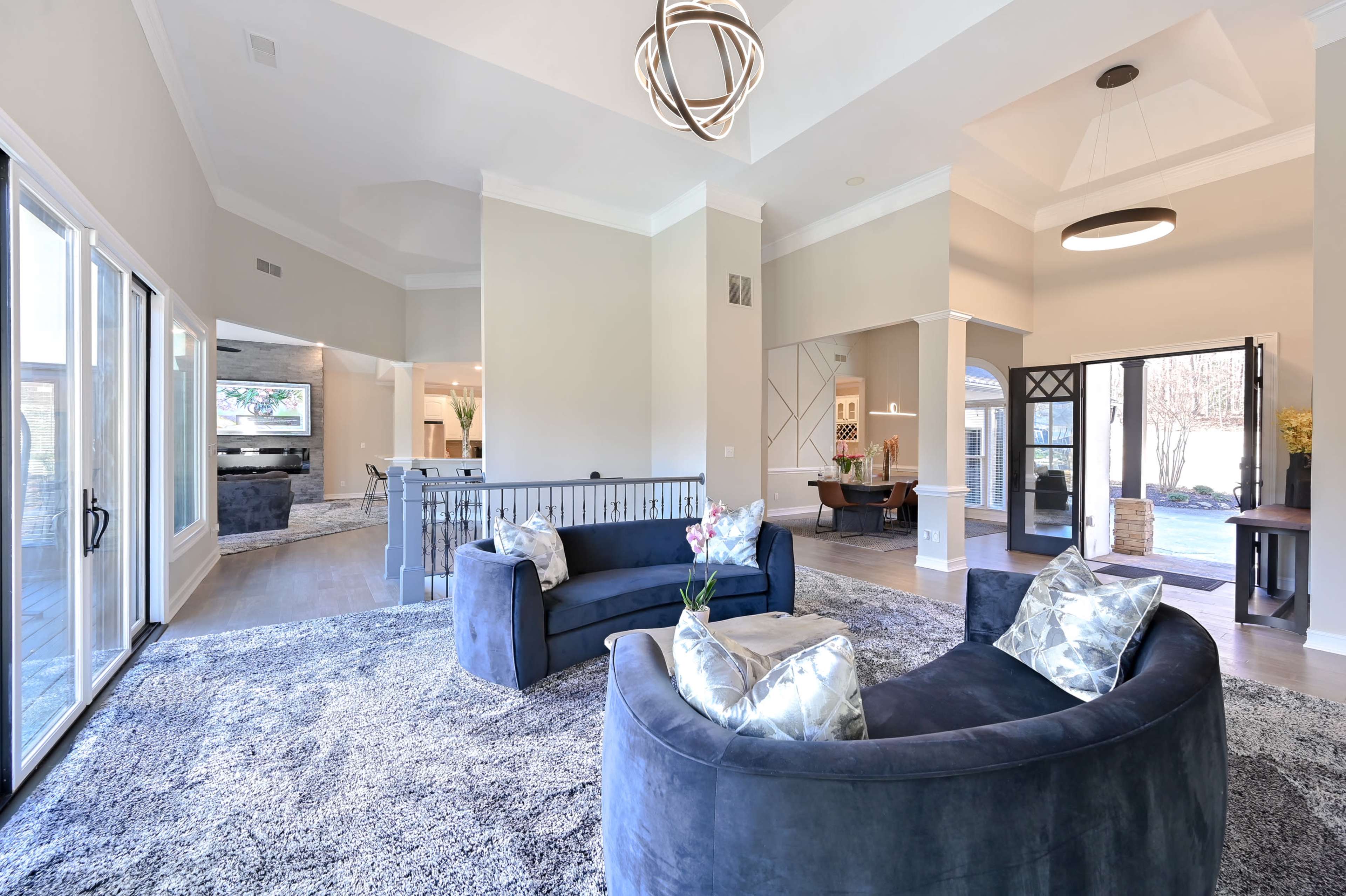 A spacious living room with two curved sofas, a large area rug, and large windows allowing natural light to fill the space.