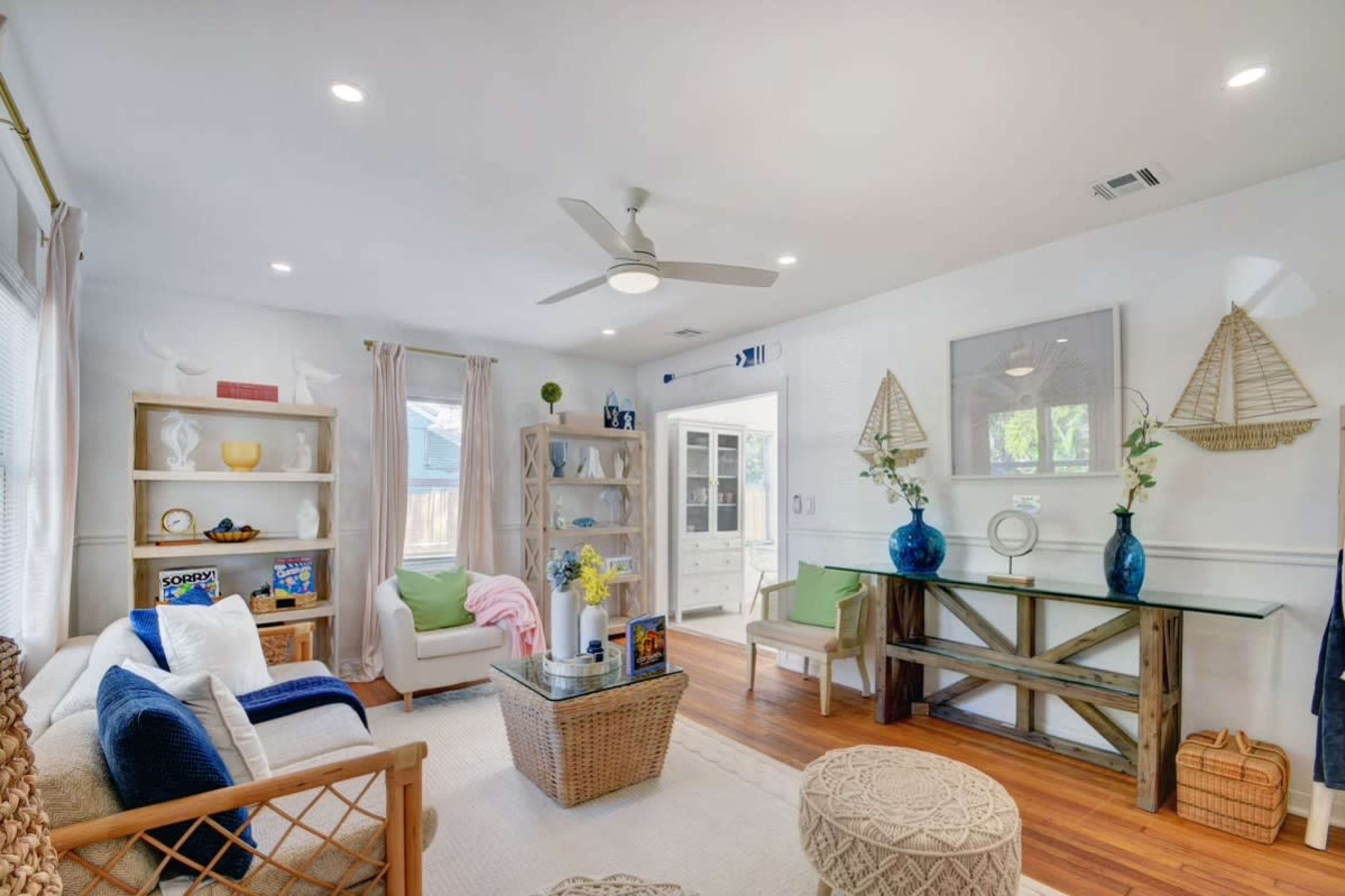 A bright living room features a sofa, woven chairs, a coffee table, and shelves adorned with decorative items.