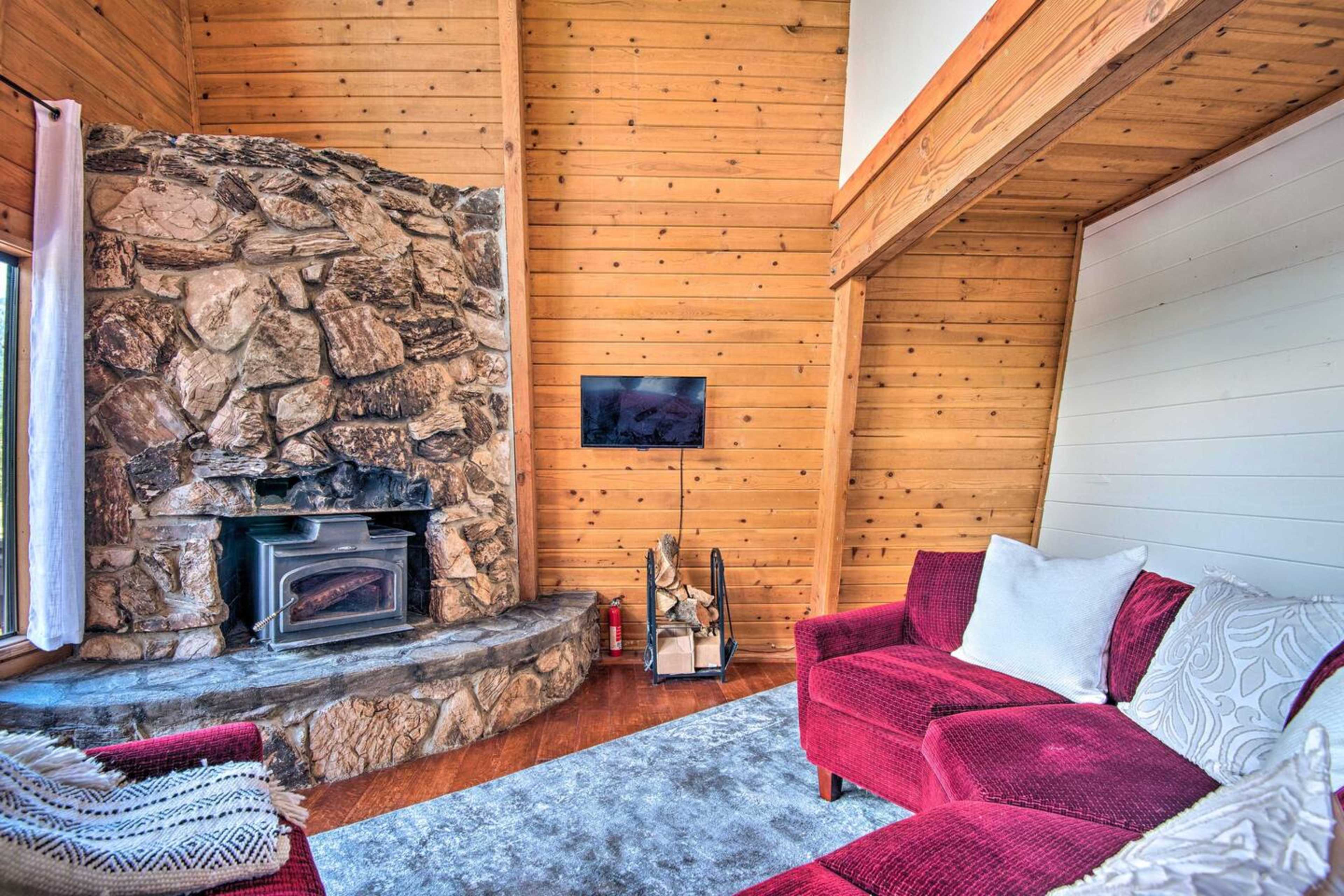 A cozy living room featuring a stone fireplace, a red upholstered sofa, and wooden walls.