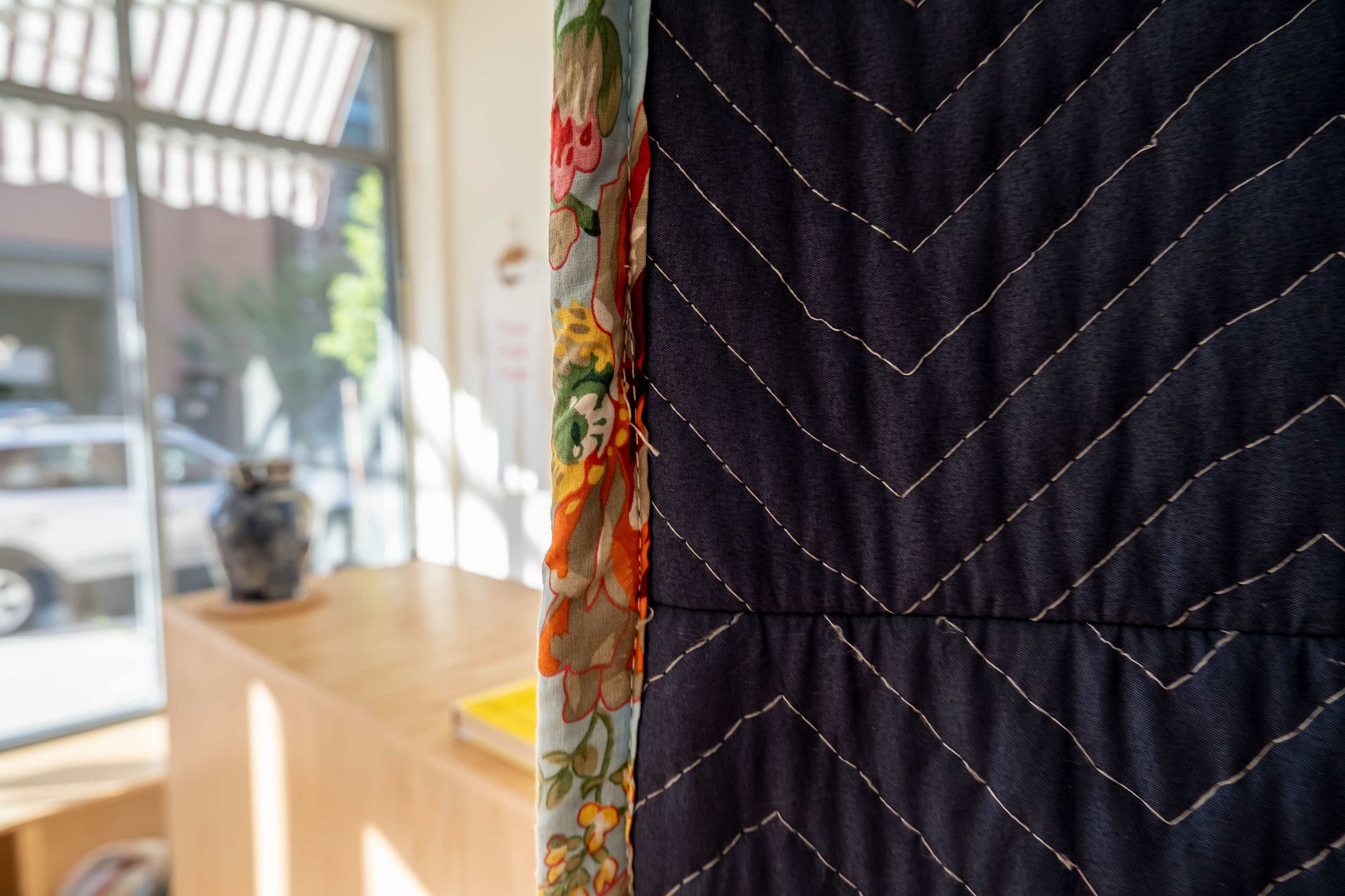 A quilted divider hangs between a bright room with a wooden surface and a window showing a street view.