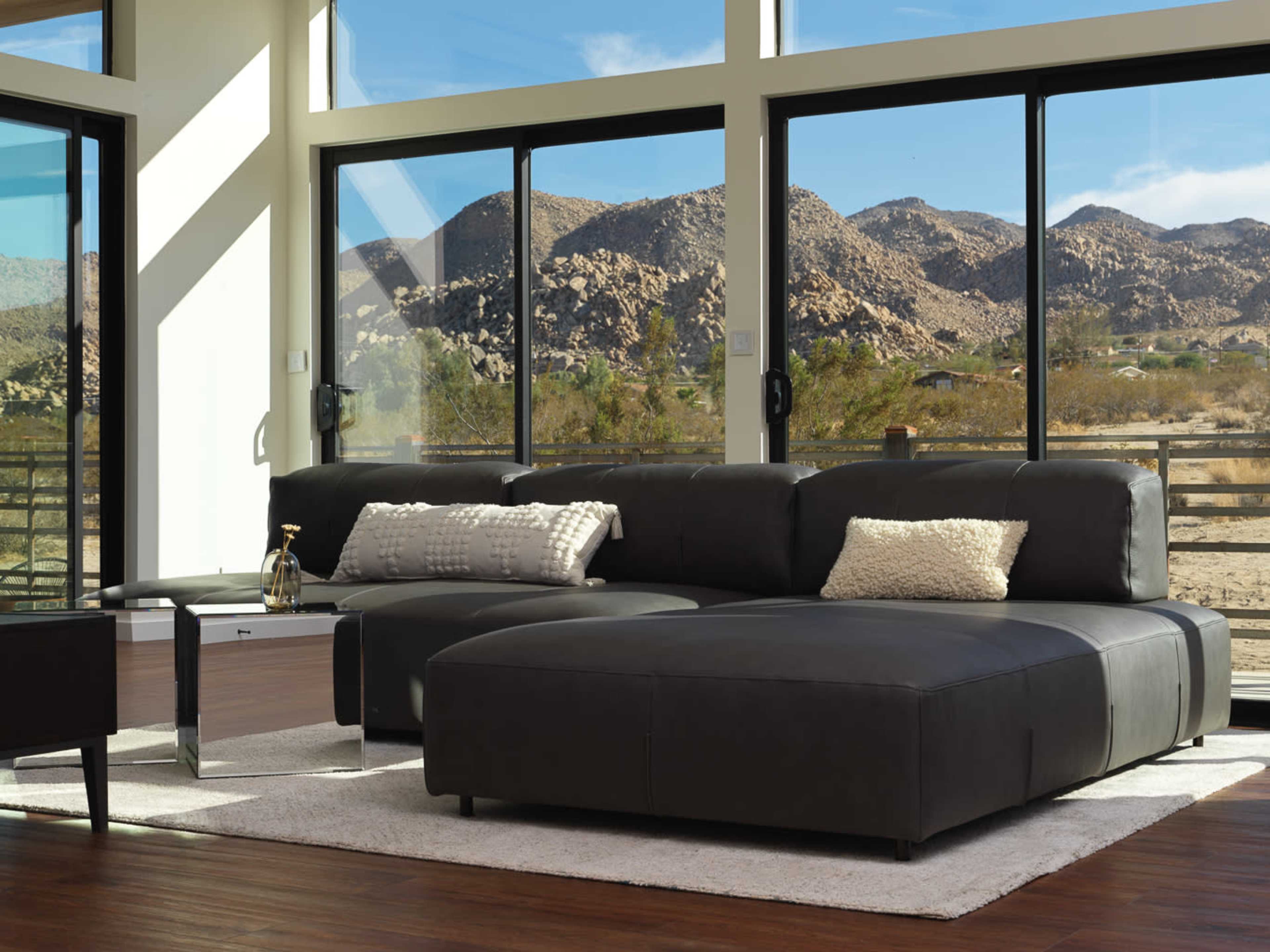 The image shows a modern living room with a dark sectional sofa and large windows overlooking a mountainous landscape.