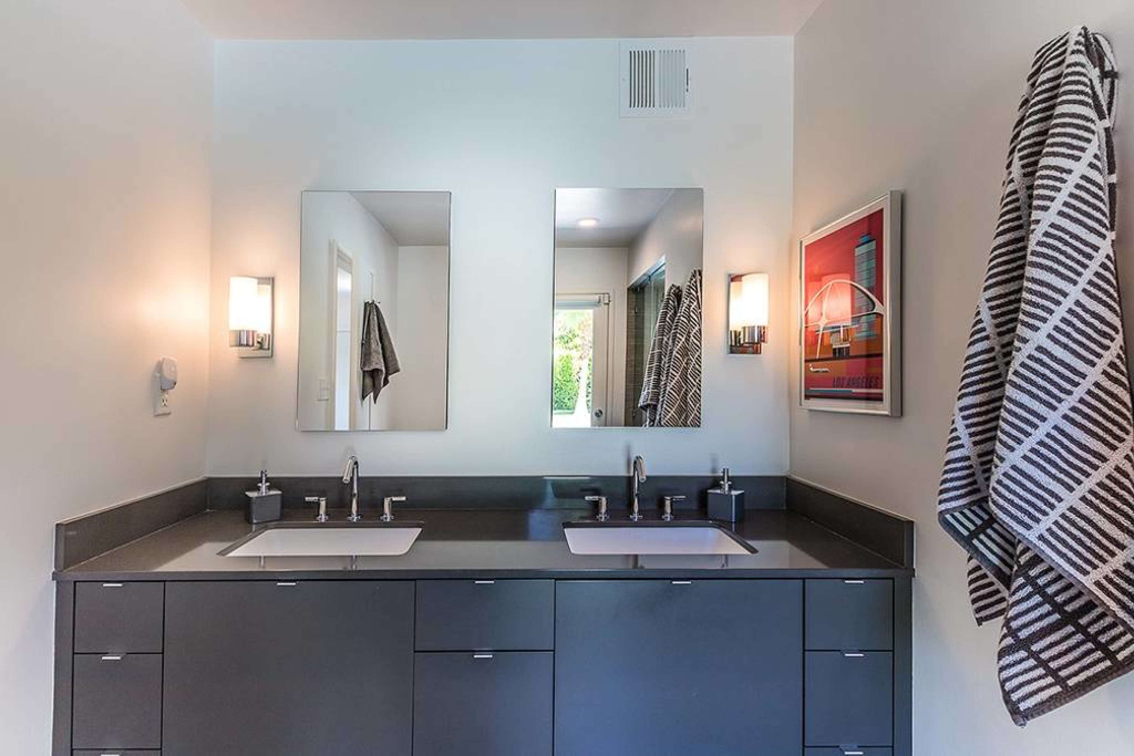 A modern bathroom features a double vanity with two sinks, two mirrors, and a towel hanging on the wall.