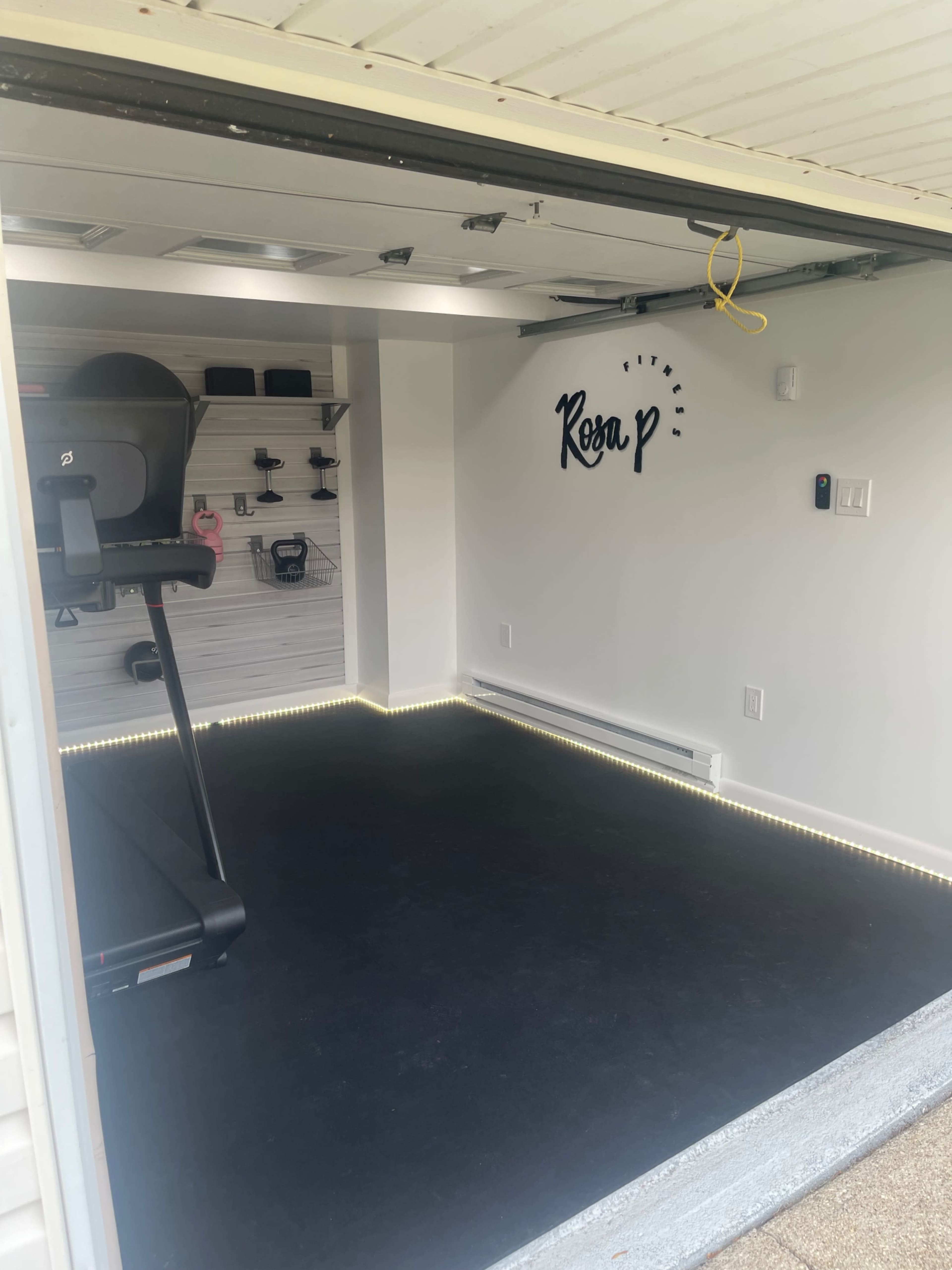 A clean, empty garage space with a treadmill and a wall featuring the name "Rosa P."
