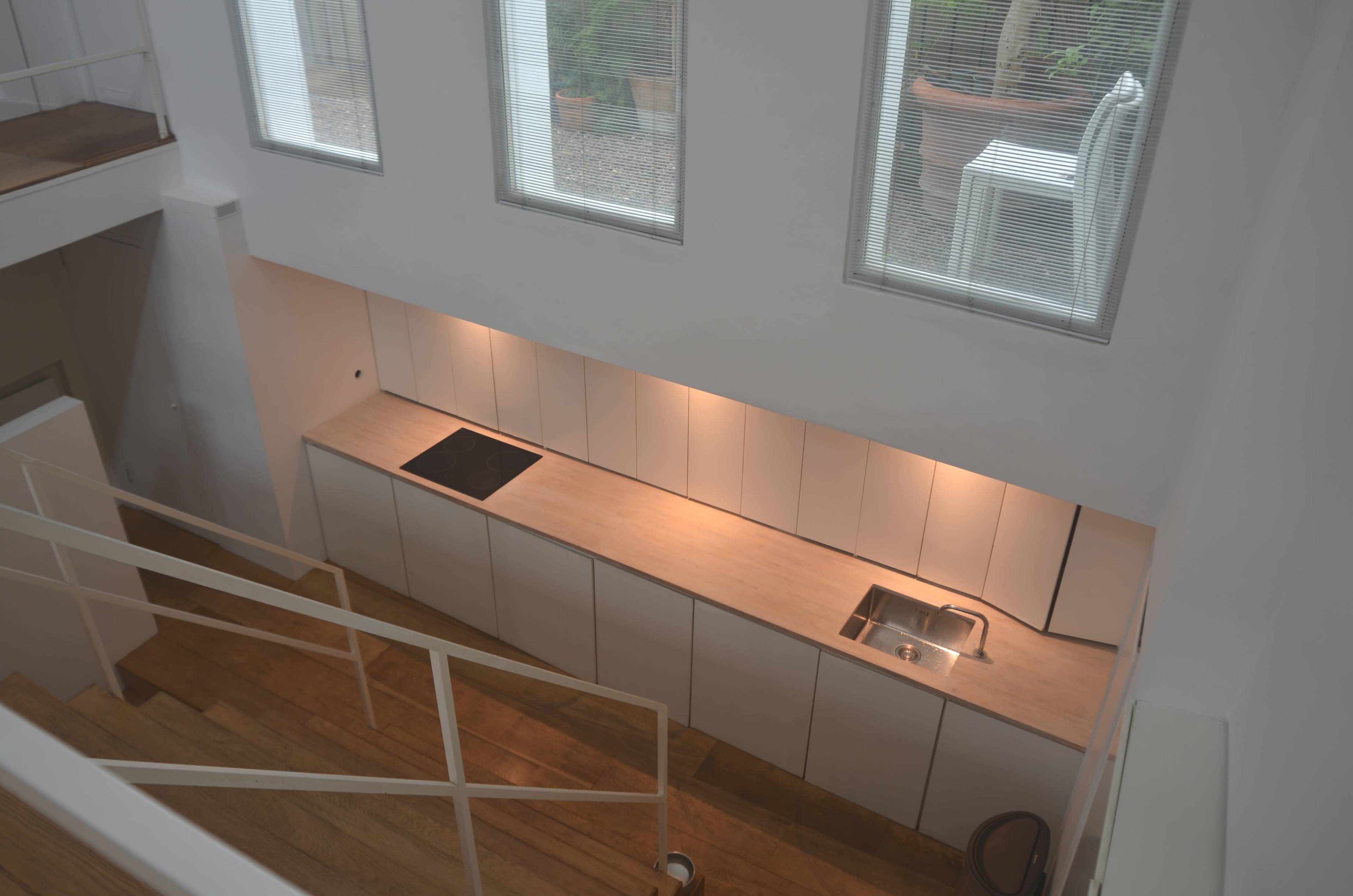 The image shows a modern kitchen with a streamlined countertop, built-in sink, and a cooktop, illuminated by warm lighting beneath a row of cabinets.