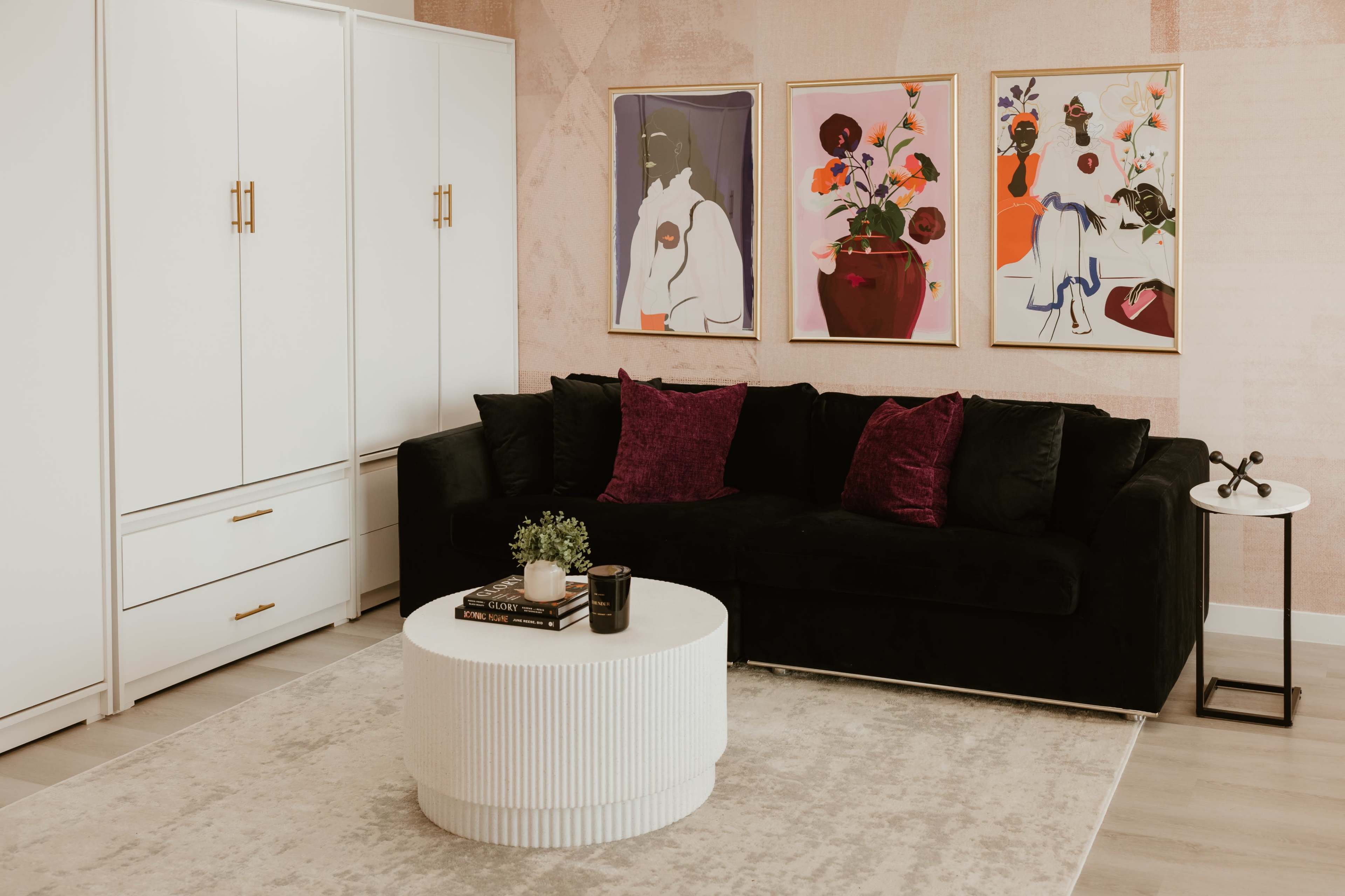 The image shows a modern living room with a black couch, a round white coffee table, and framed artwork on the wall.