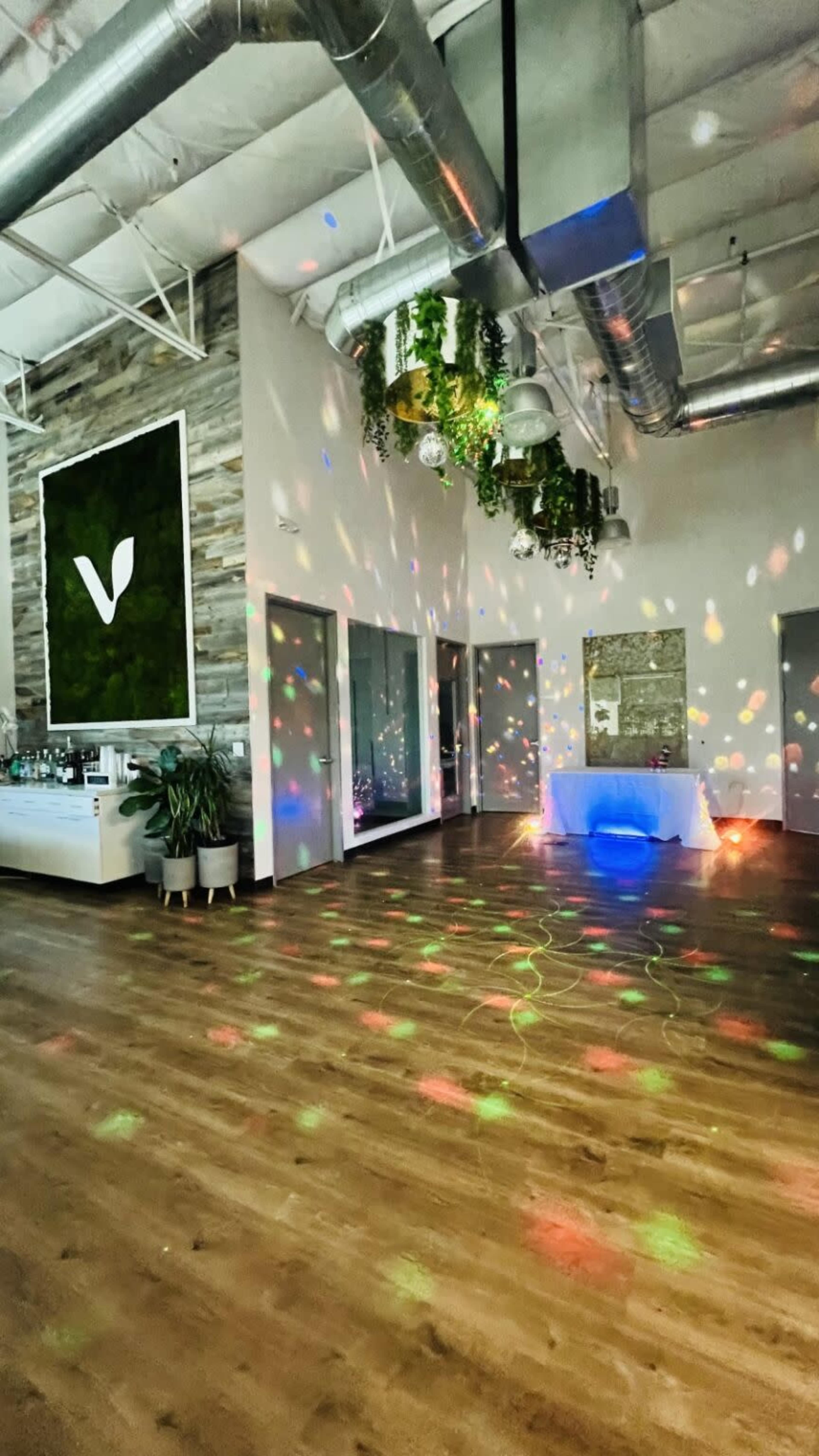 The image shows an indoor venue with a wooden floor, colorful lights reflecting off the walls and ceiling, and a bar area in the background.