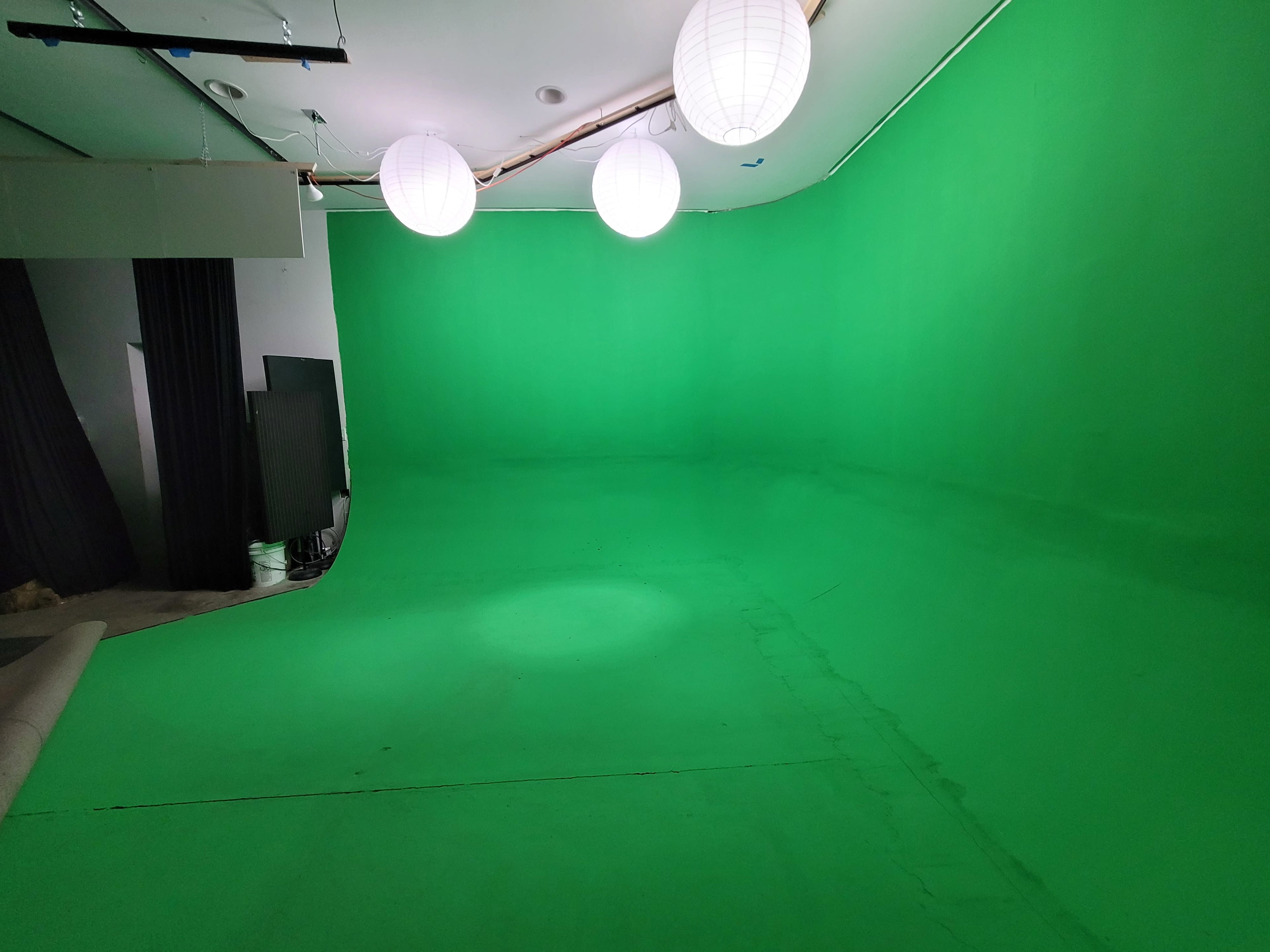 The image shows a green screen studio with a smooth green backdrop and three round light fixtures hanging from the ceiling.