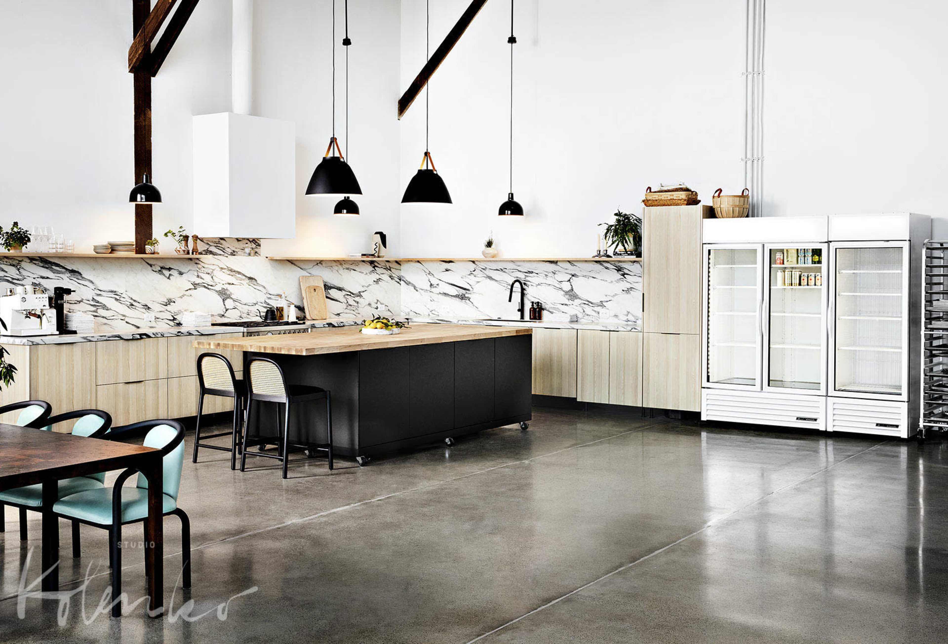 A modern kitchen with a large island, black and wooden cabinetry, marble backsplash, and a glass-front refrigerator.