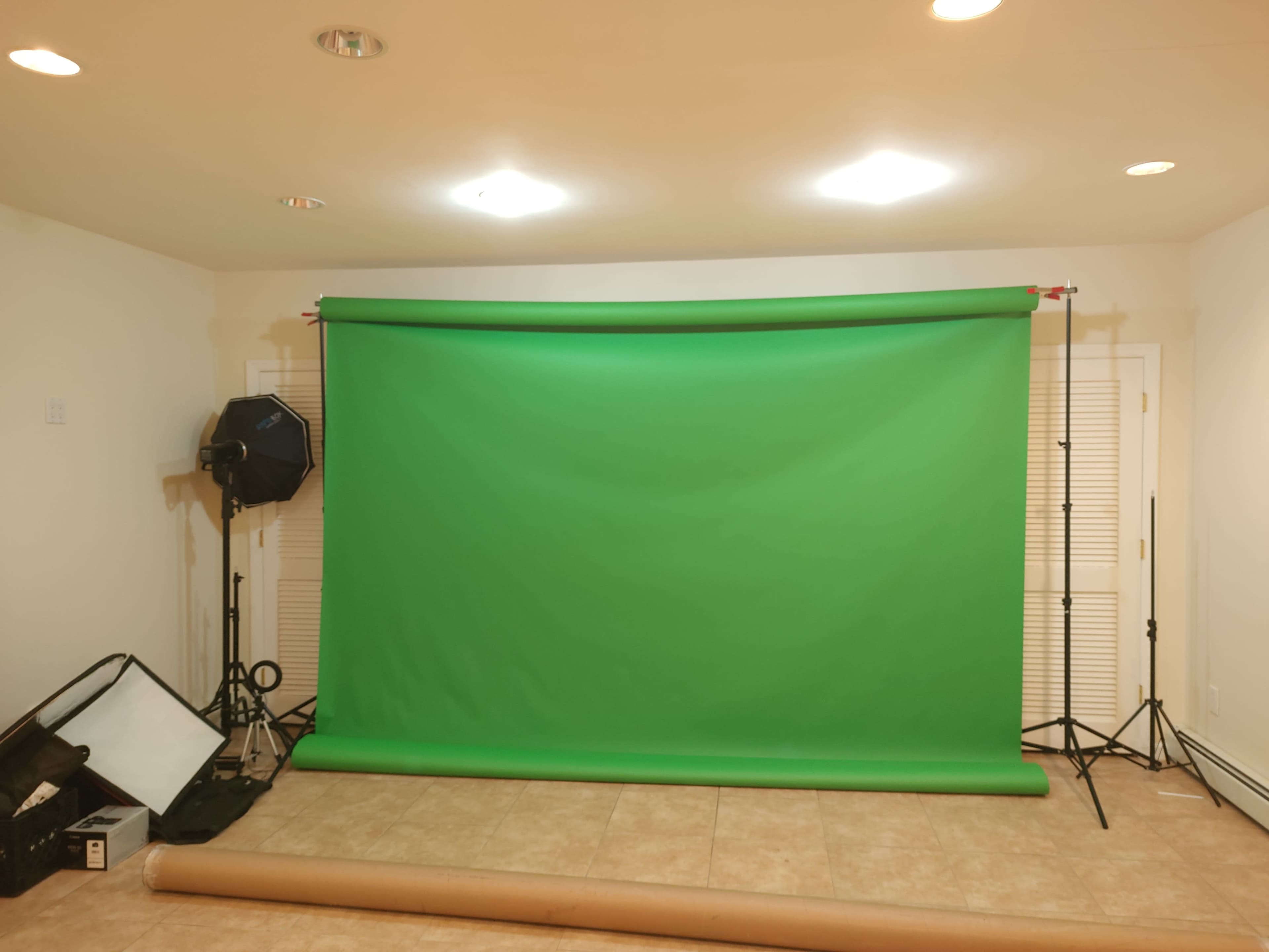 A green backdrop set up in a room with lighting equipment and materials scattered on the floor.