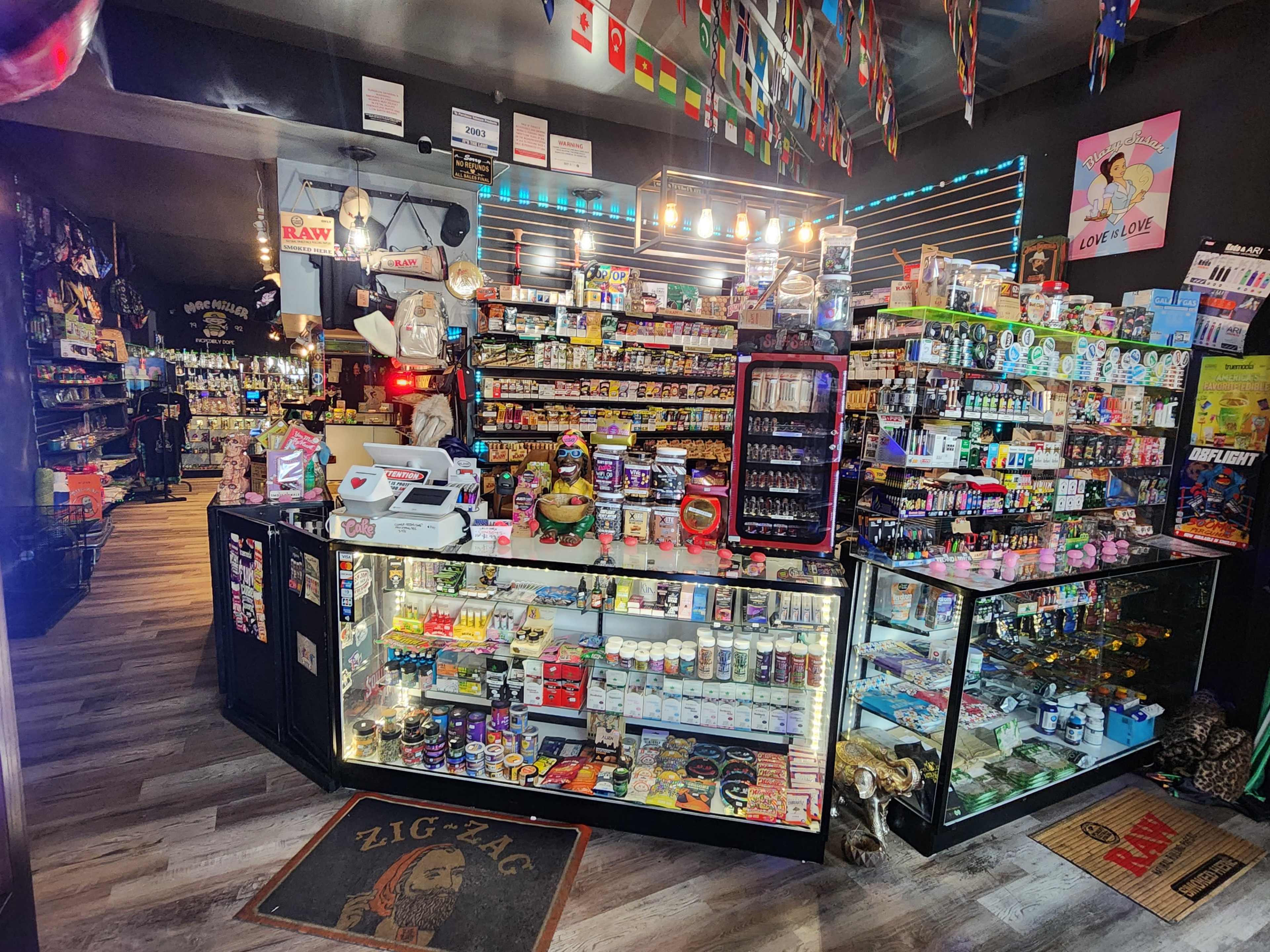 The image shows a convenience store interior filled with a variety of snacks, drinks, and merchandise displayed on shelves and counters.
