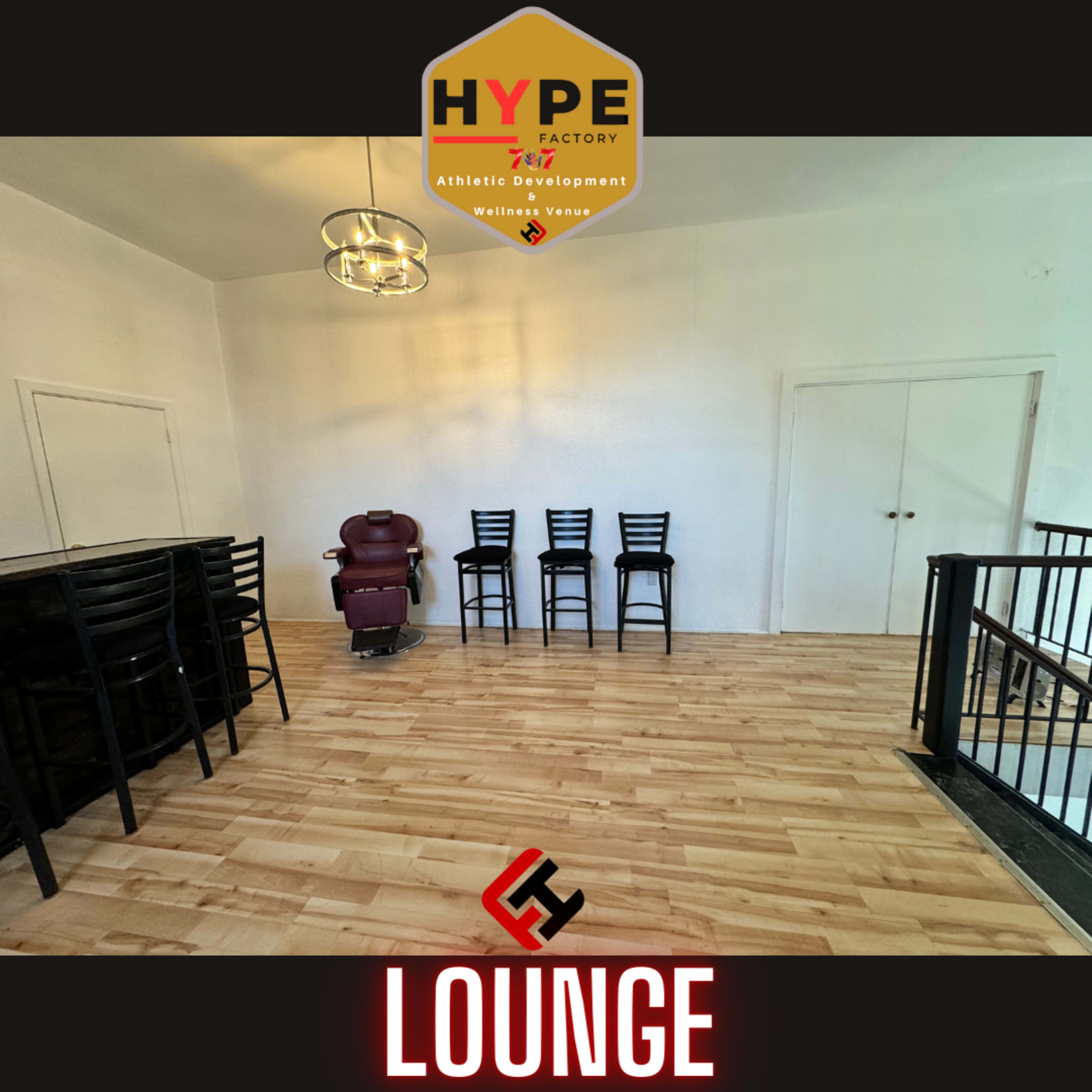 A spacious lounge area with wooden flooring, a few black chairs, and a massage chair against a plain white wall.