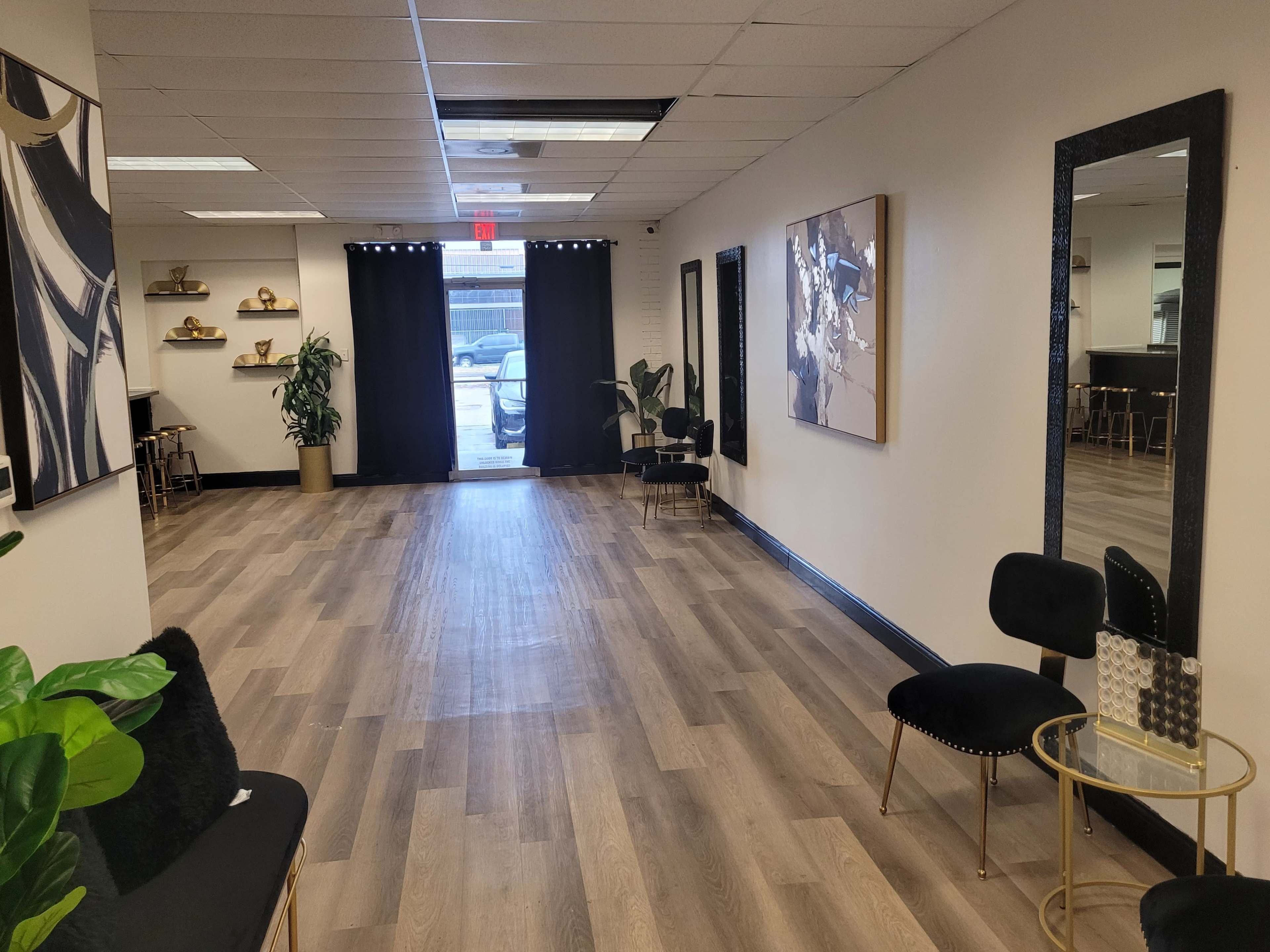 The image shows a spacious, well-lit hallway with wooden flooring, featuring black curtains at the entrance and modern decor on the walls.