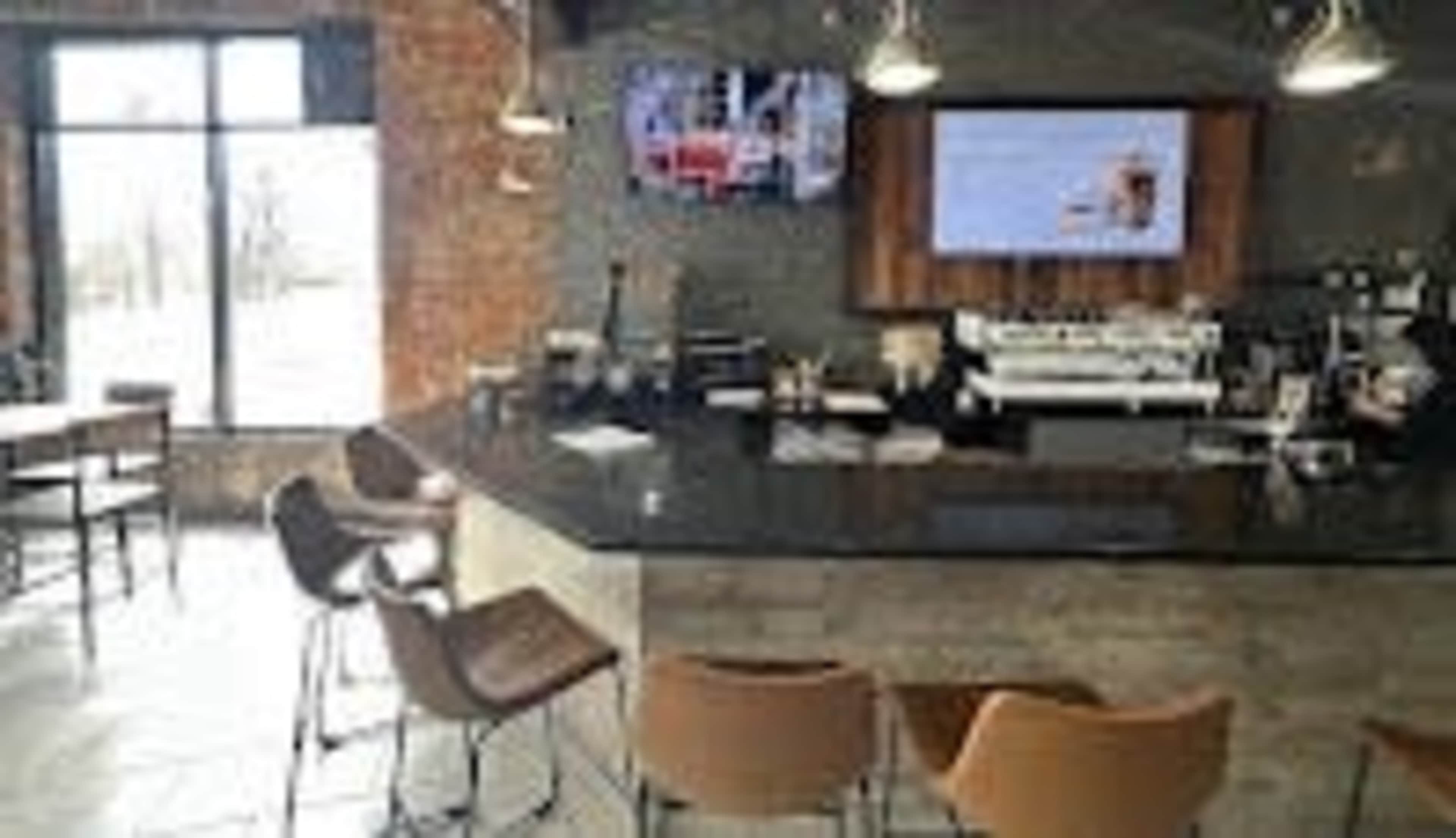 The image shows a modern café interior with a dark counter, bar stools, and large windows letting in natural light.