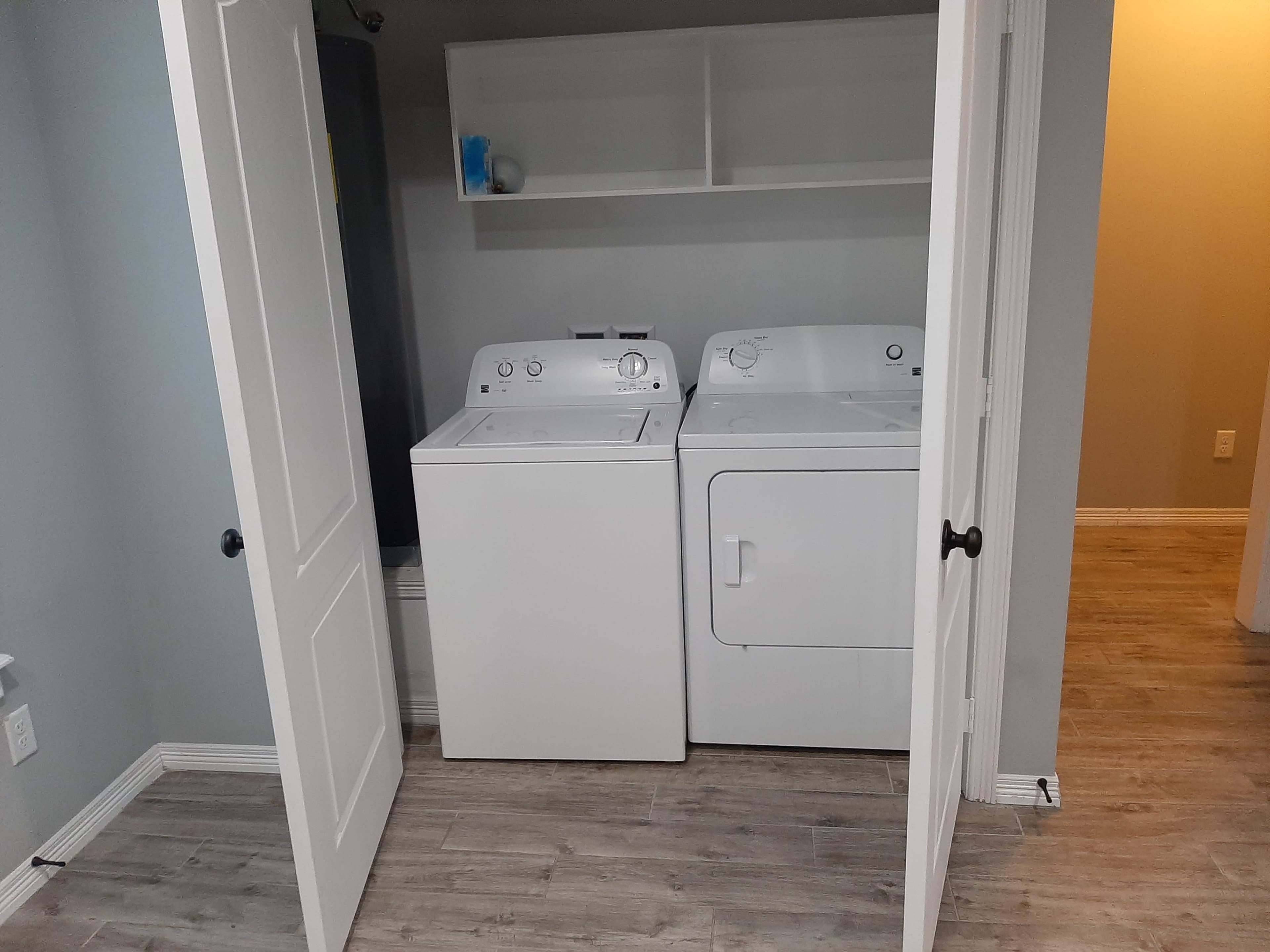The image shows a laundry room with a washer and dryer side by side, enclosed by white double doors.