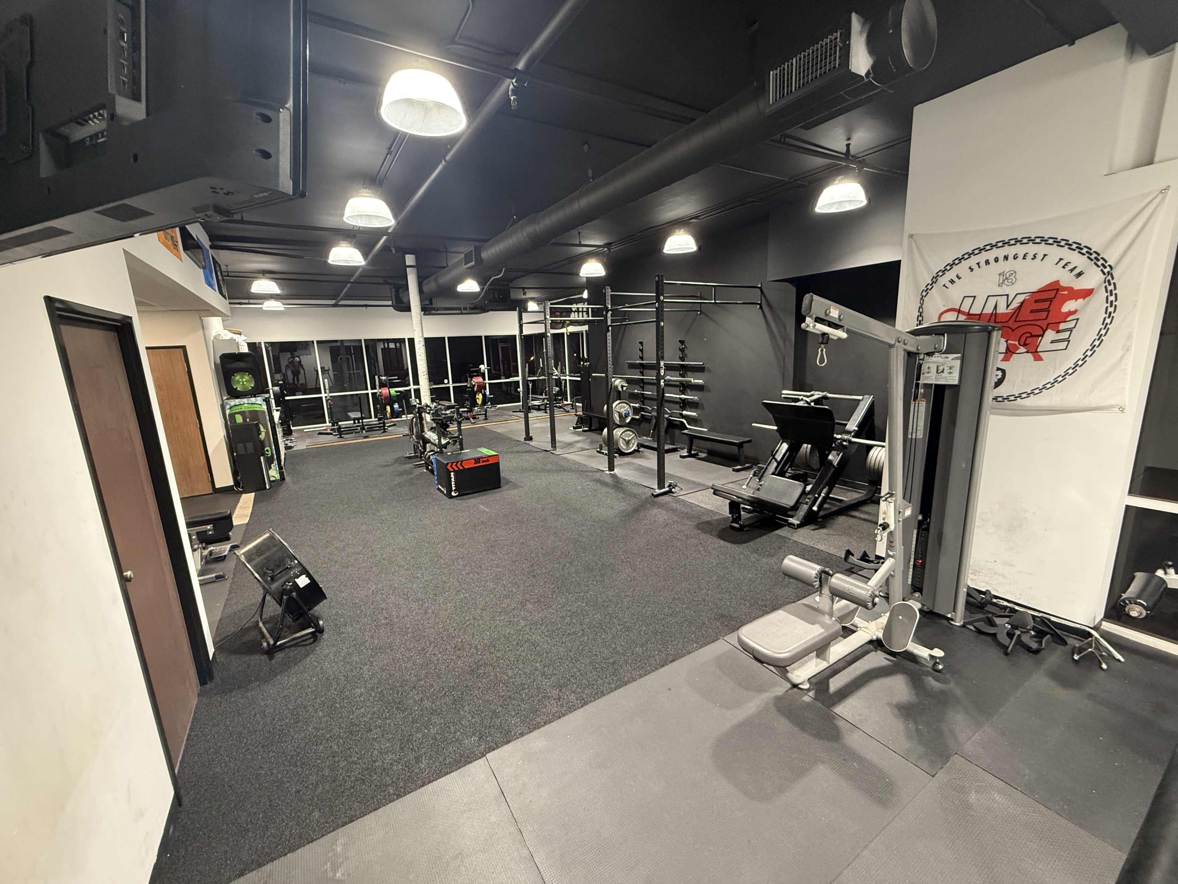 The image shows a well-equipped gym with various exercise machines, weights, and fitness equipment on a black carpeted floor.
