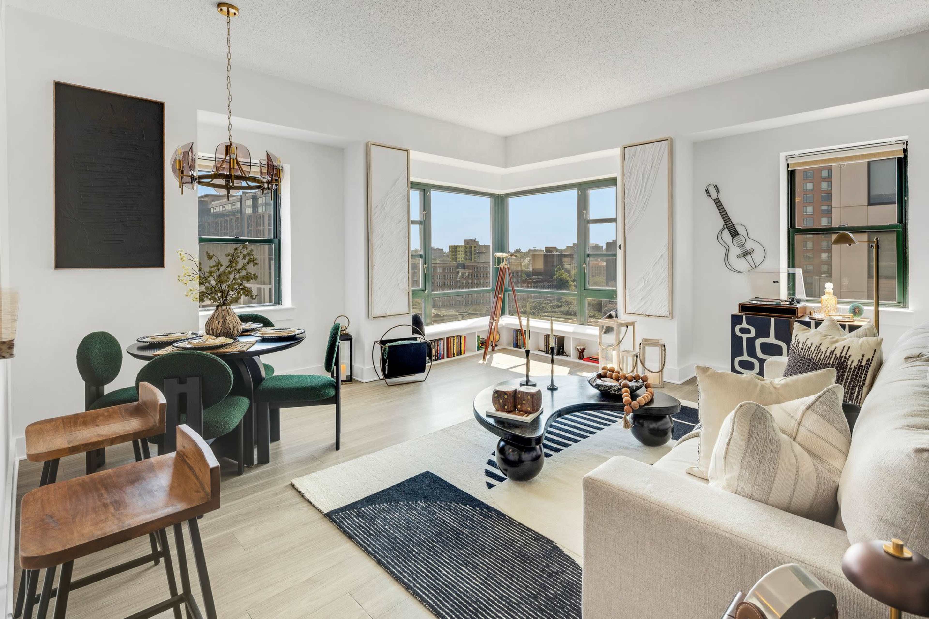 A modern living space features a dining area with a round table and chairs, a cozy seating area with a couch, and large windows offering a view of the city.