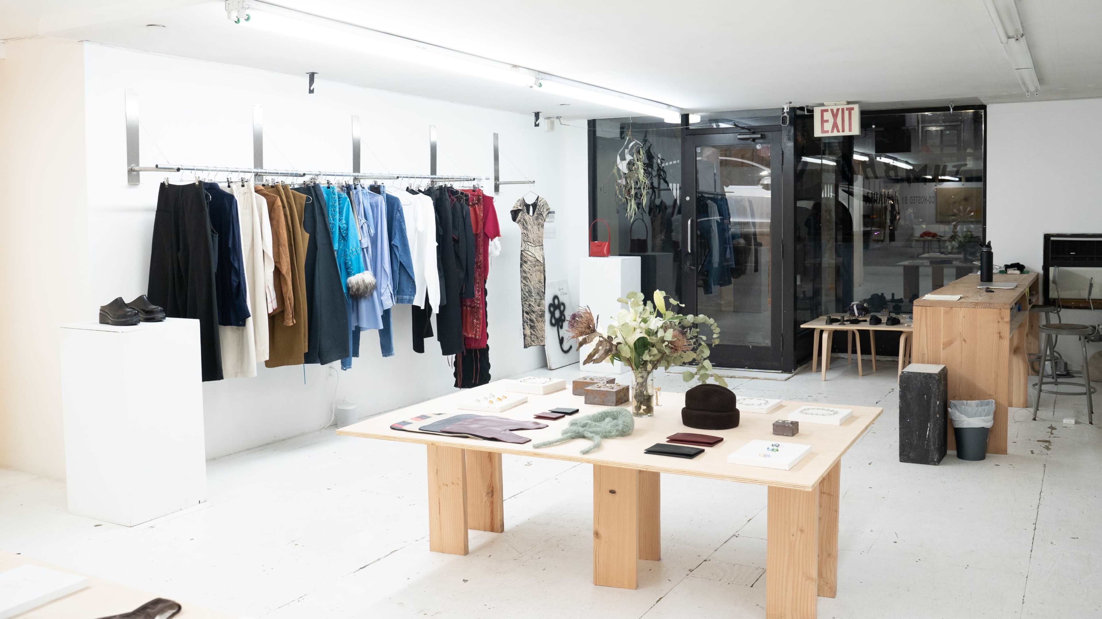 An indoor clothing boutique featuring hanging garments on racks and a display table with various fashion accessories.