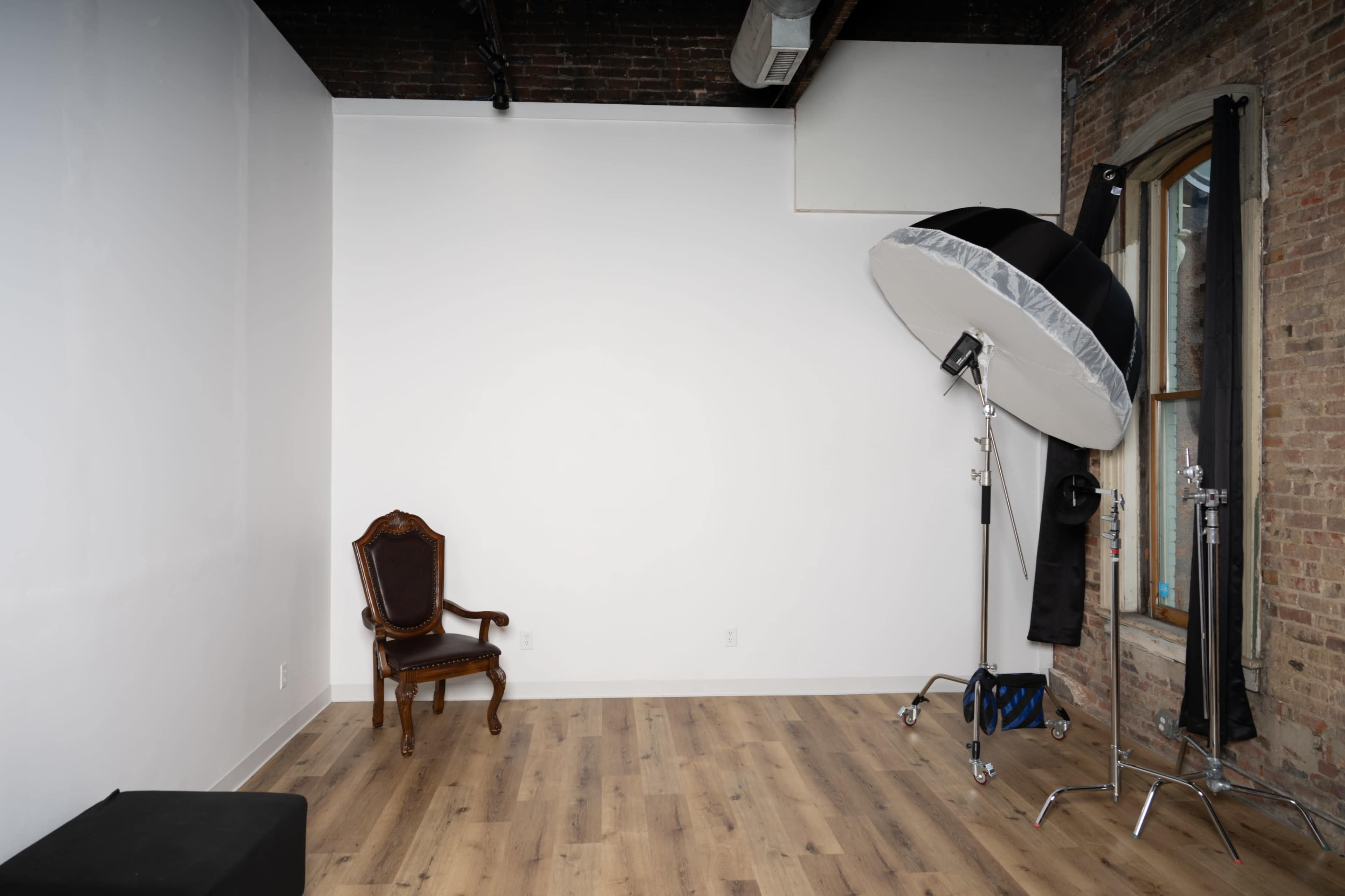 An empty studio space featuring a vintage chair and a large reflector on a stand.