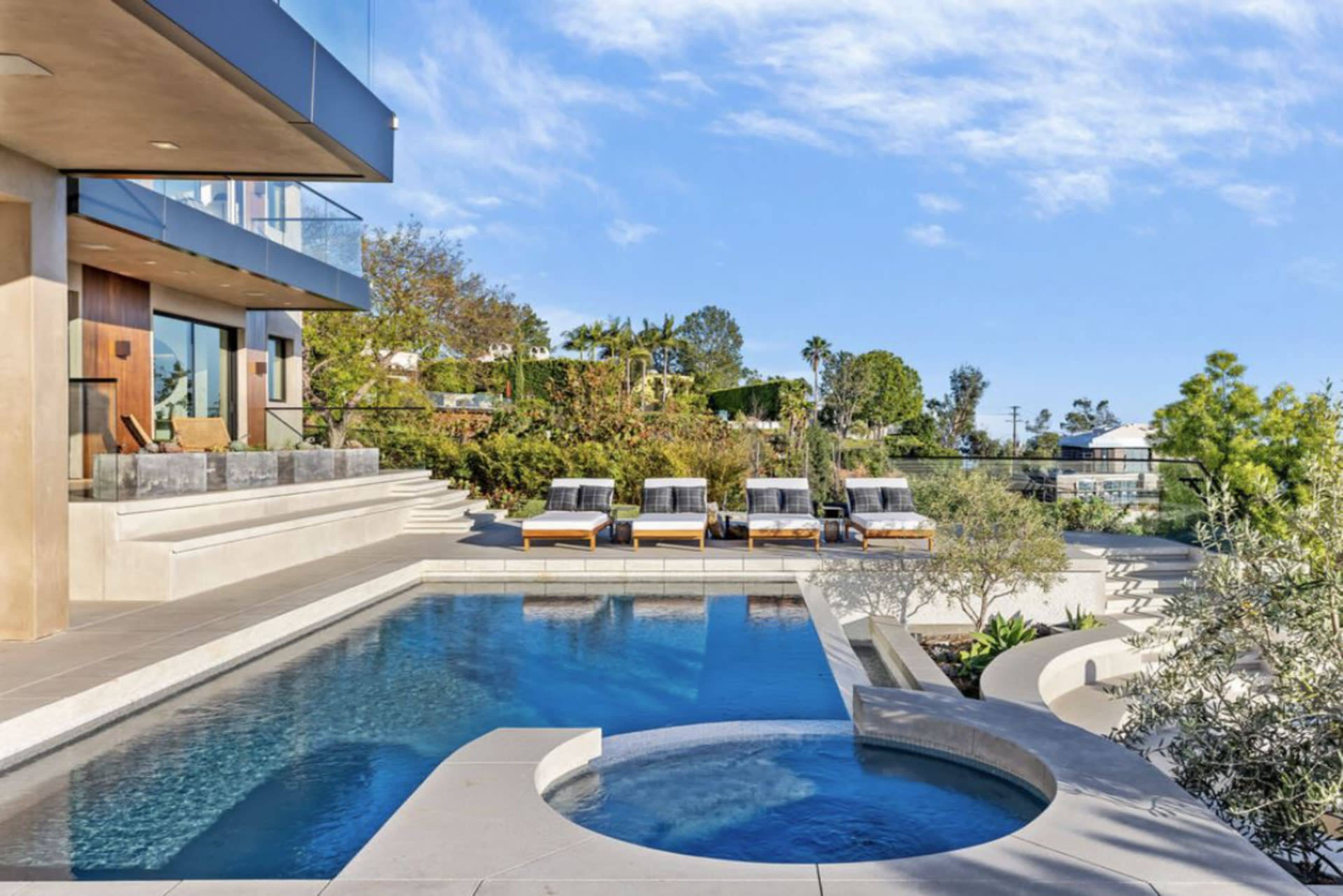 A modern house features a landscaped backyard with a swimming pool, hot tub, and lounge chairs.