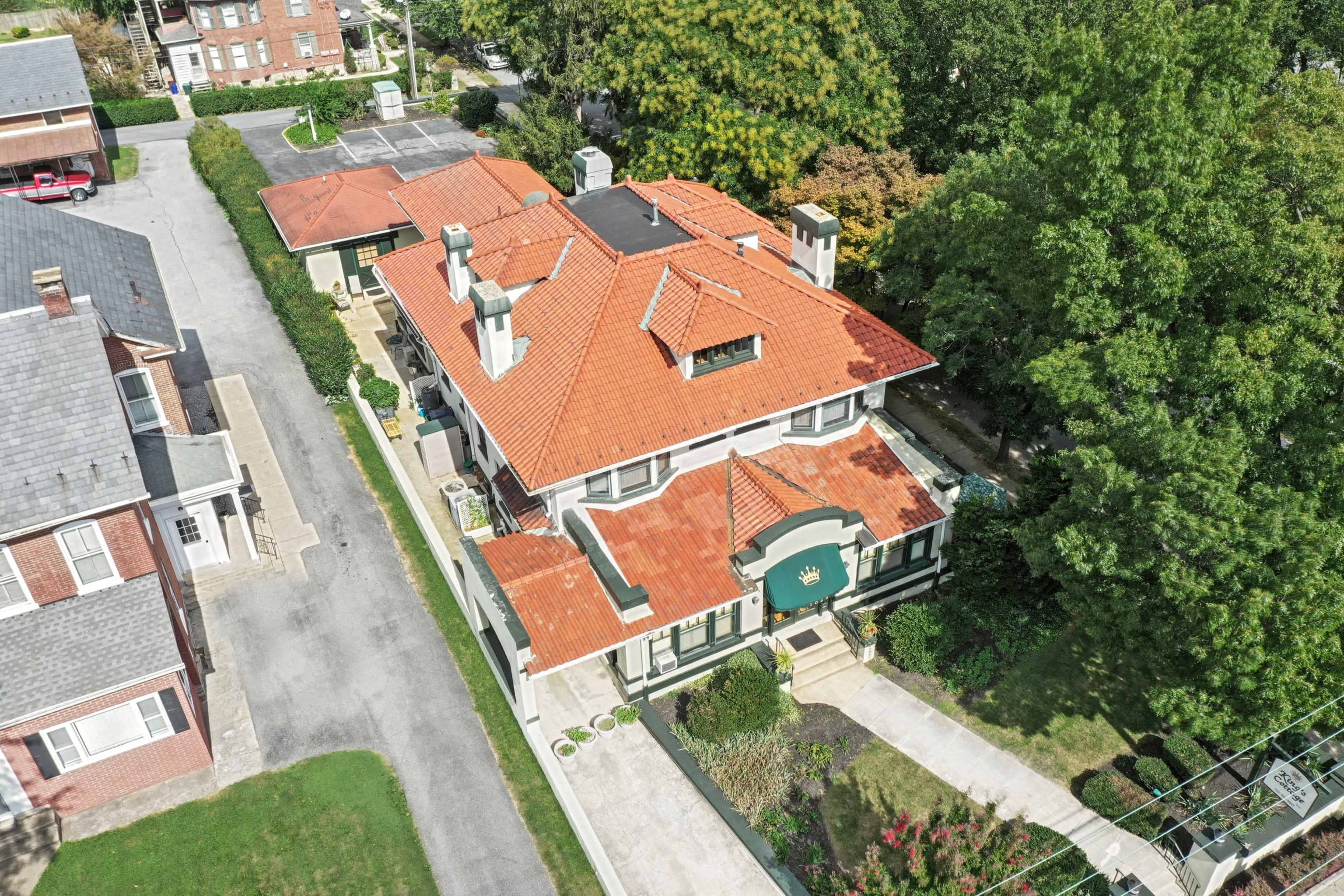 A two-story house with a red tile roof, surrounded by greenery and neighboring buildings.