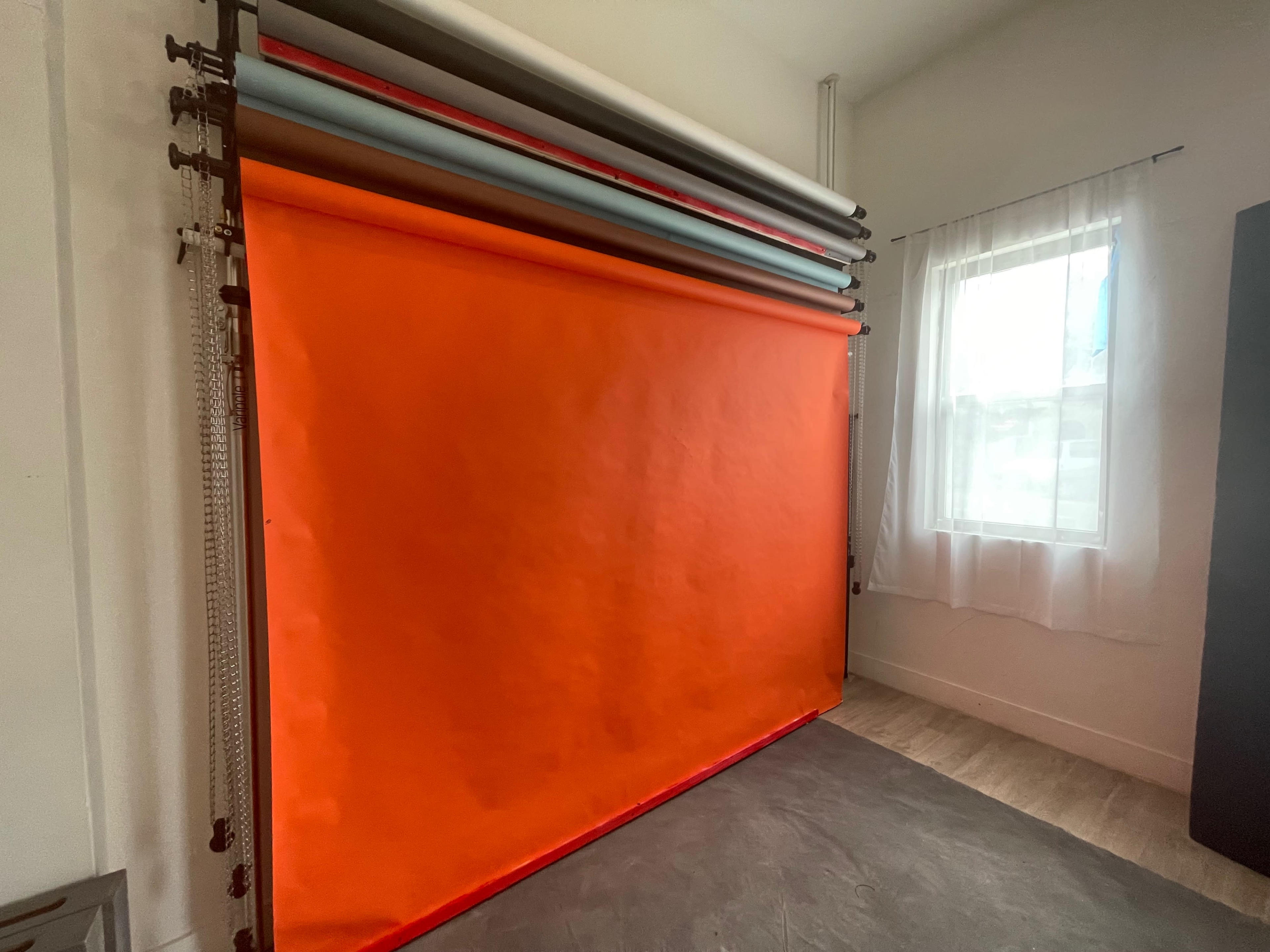 A bright orange backdrop set up in a room with natural light coming through a window.