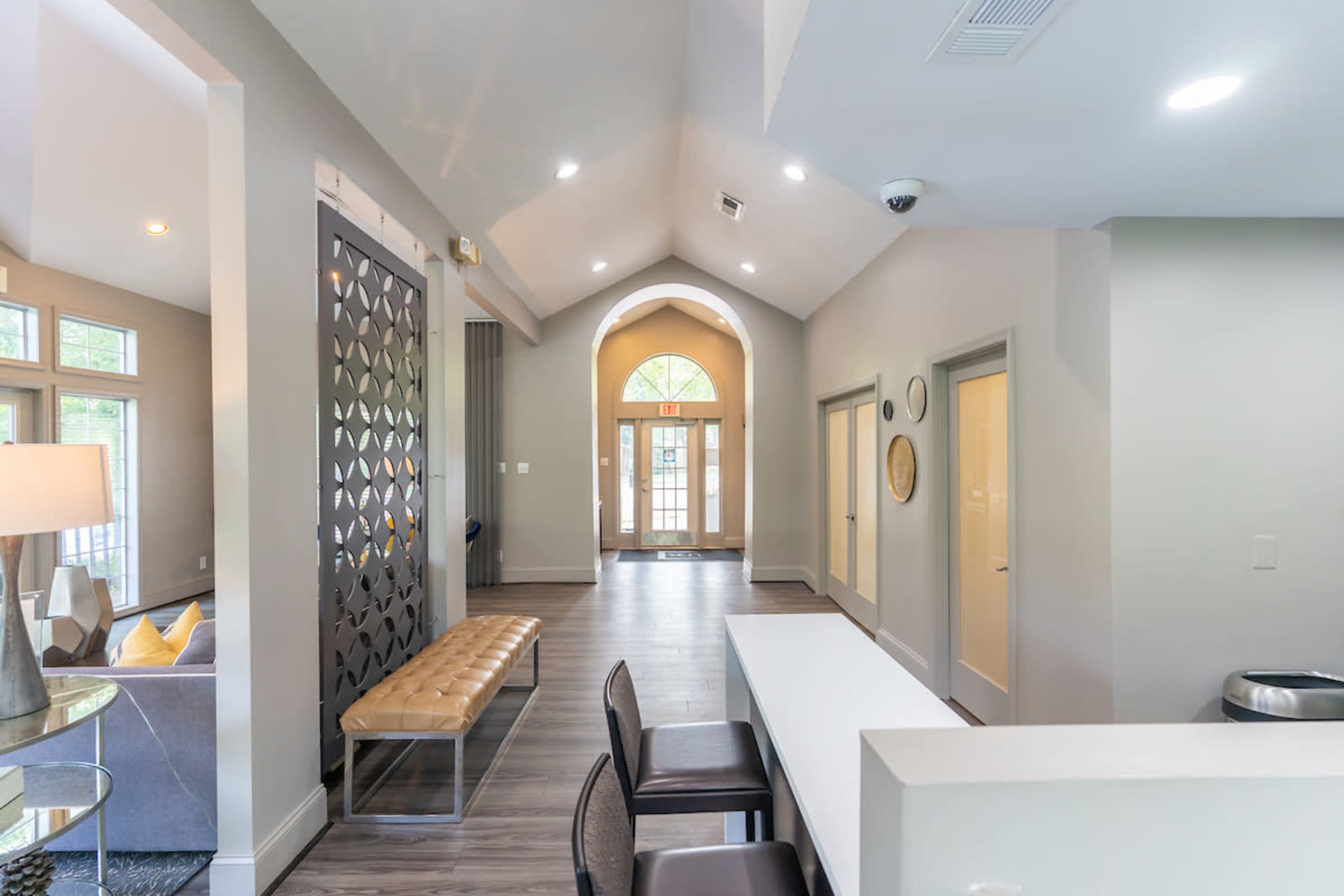 A modern interior space with high ceilings, a bench, and an entrance door framed by large windows.