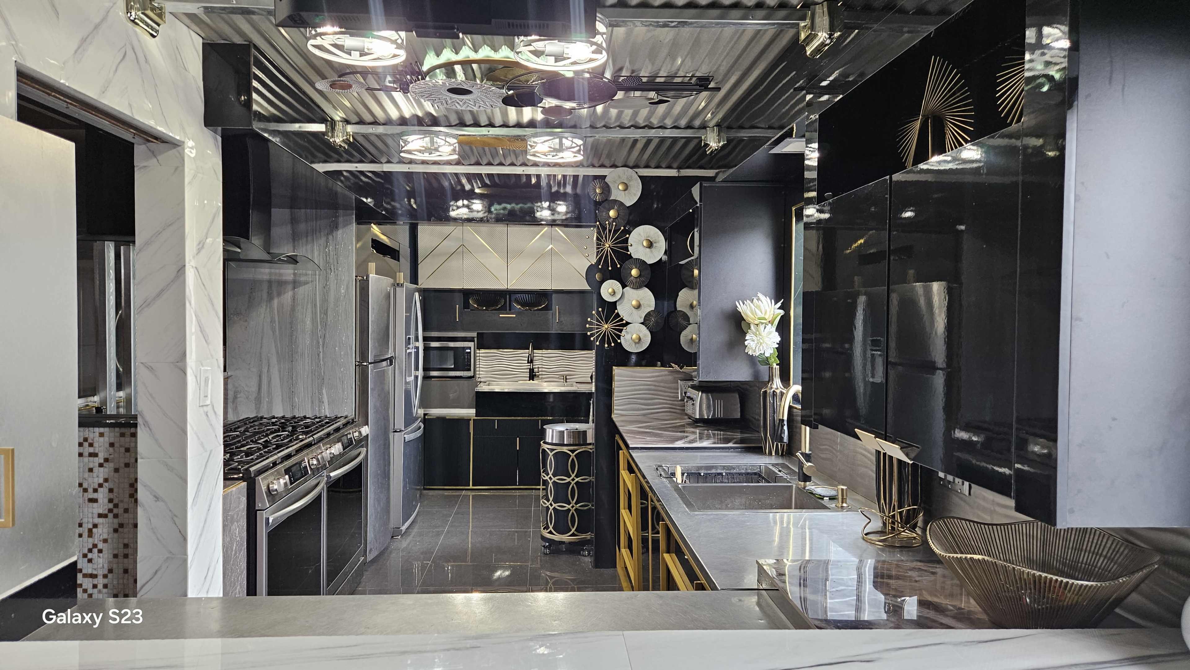 The image shows a modern kitchen featuring sleek black cabinetry, stainless steel appliances, and decorative metallic accents.