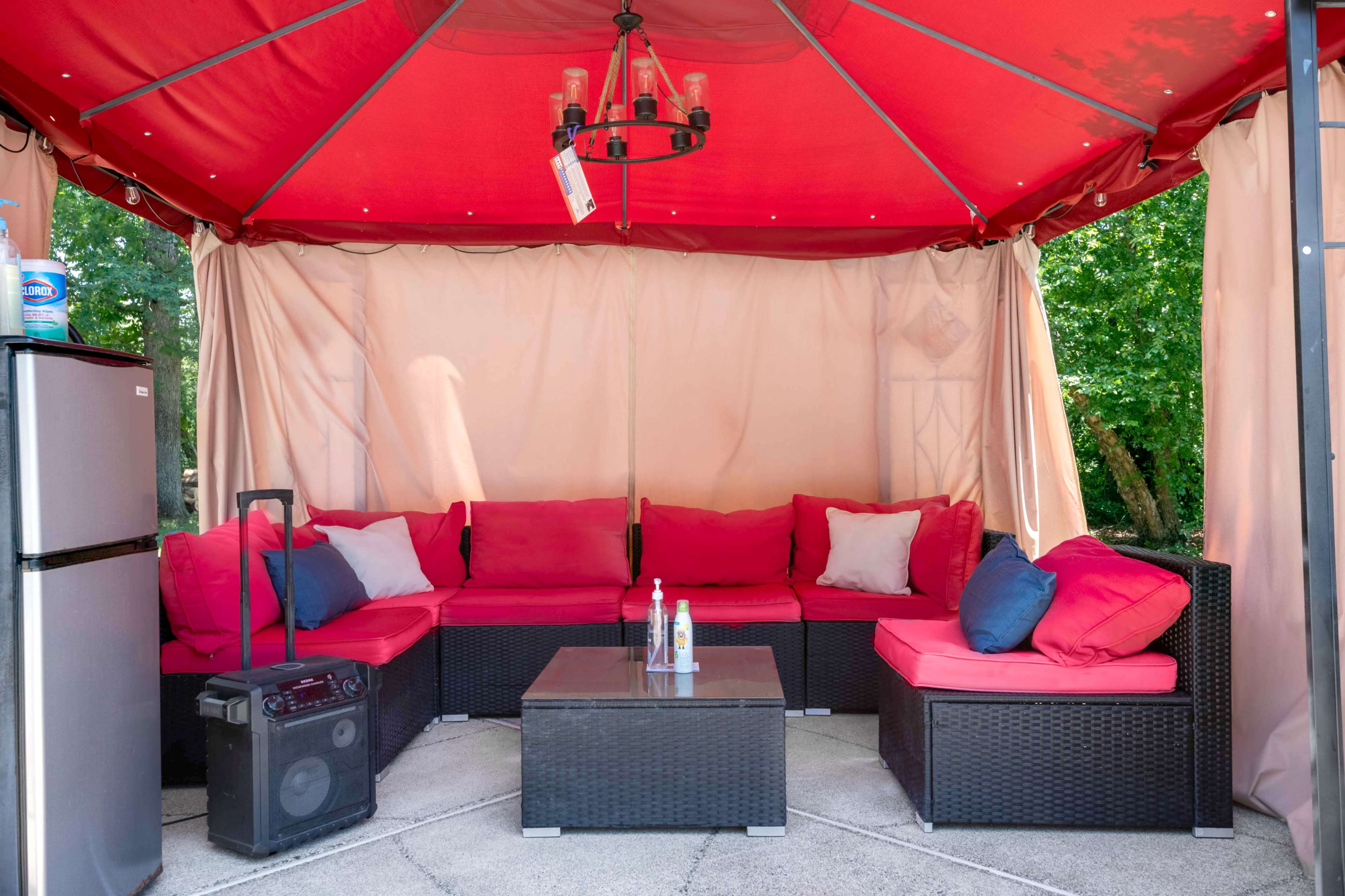 A covered outdoor seating area with a red canopy, brown wicker furniture, and a table in the center.