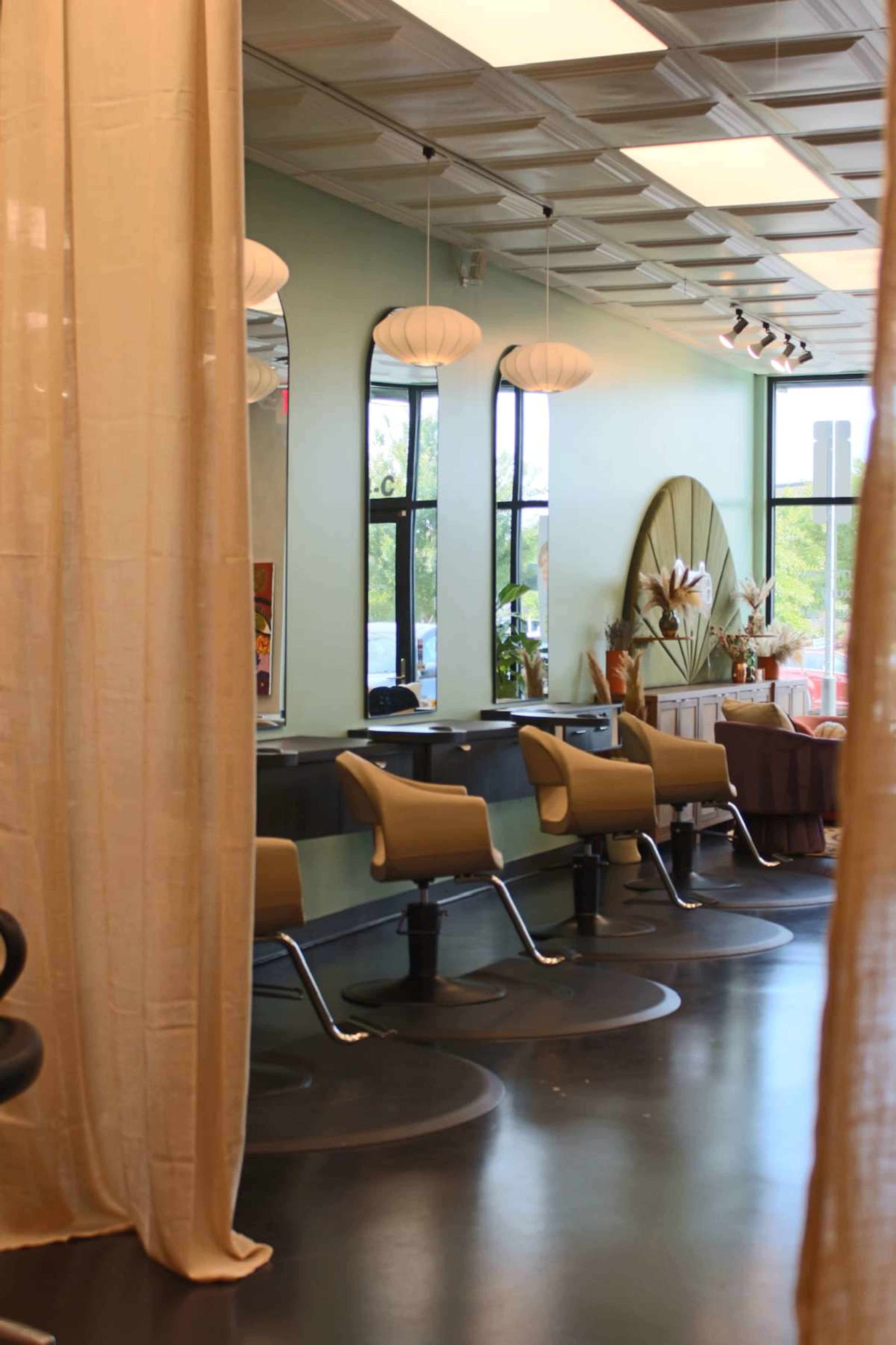 The image shows the interior of a hair salon with styling stations, light green walls, and soft lighting, separated by fabric curtains.