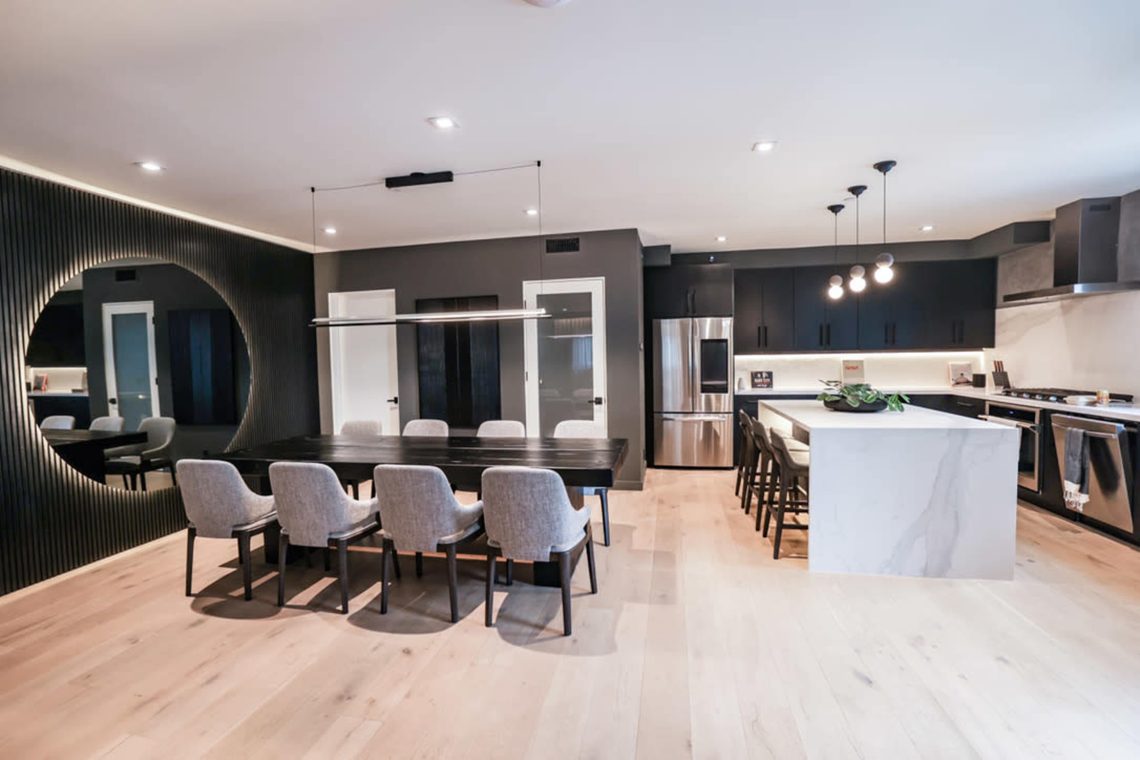 A modern kitchen and dining area featuring a sleek black and white color scheme, with a large dining table set for eight next to a kitchen island with bar seating.