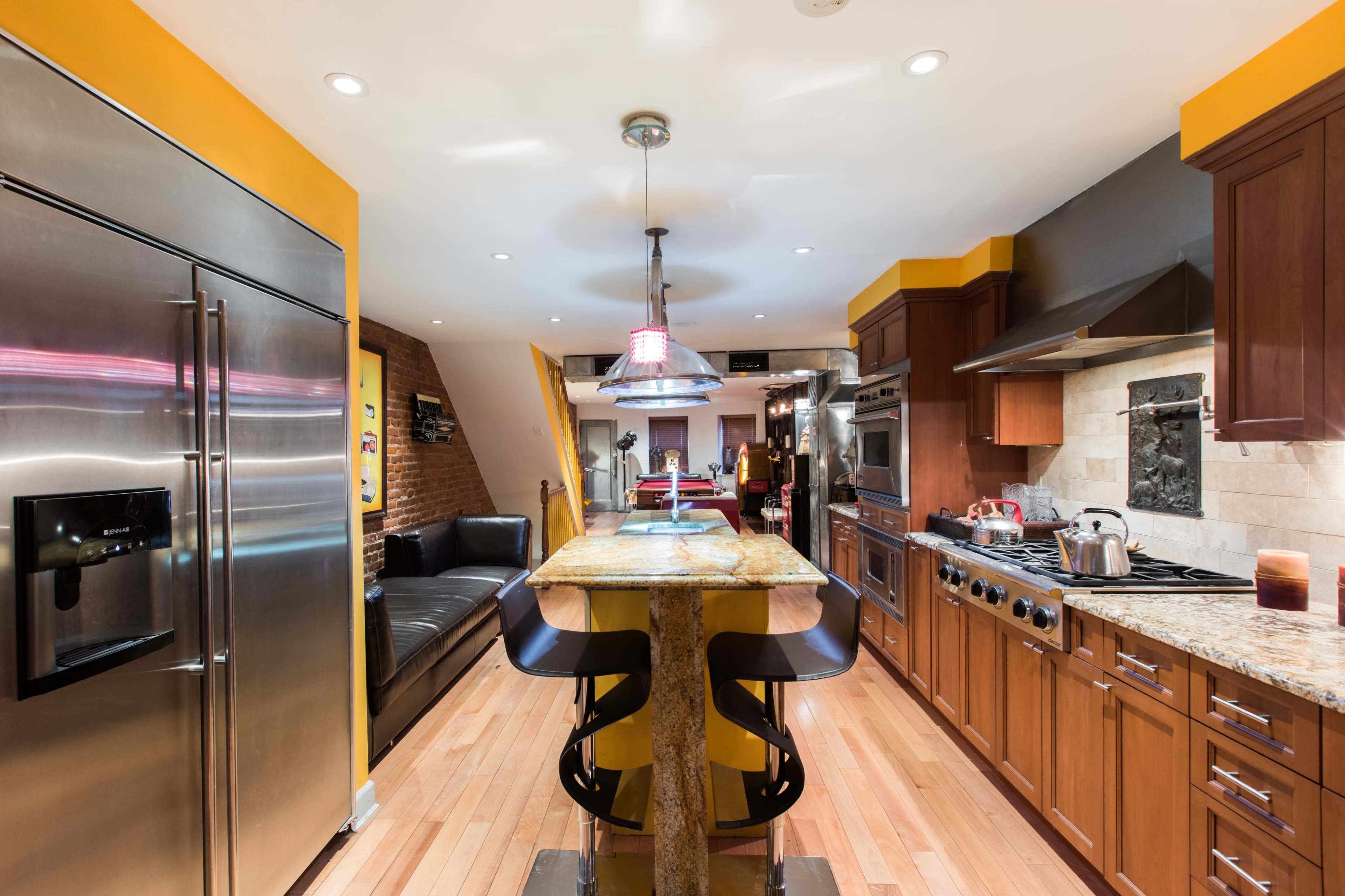 A modern kitchen featuring a central island with yellow accents, stainless steel appliances, and wooden cabinetry.