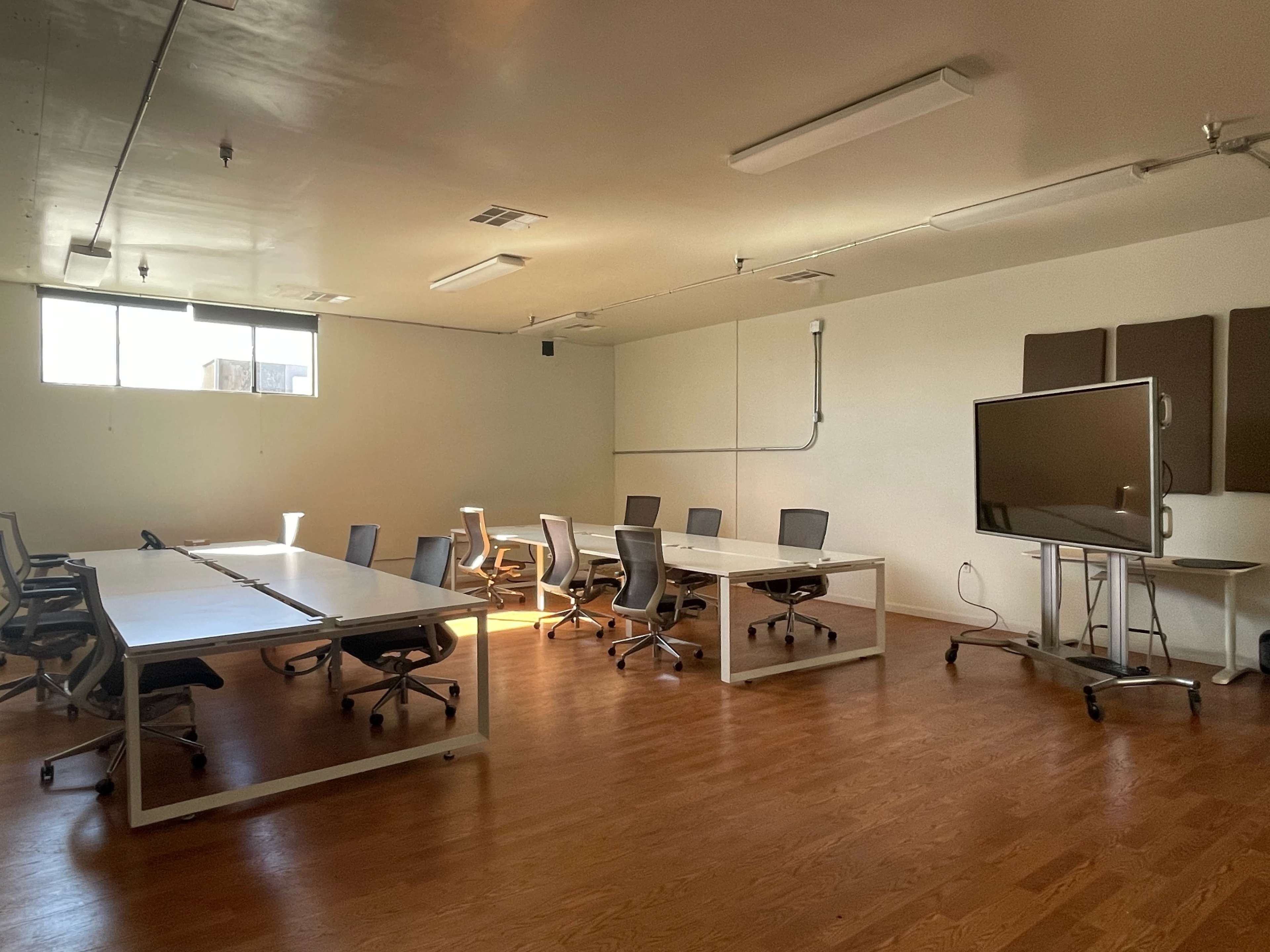 A spacious conference room features multiple tables and chairs, along with a large screen and hardwood flooring.