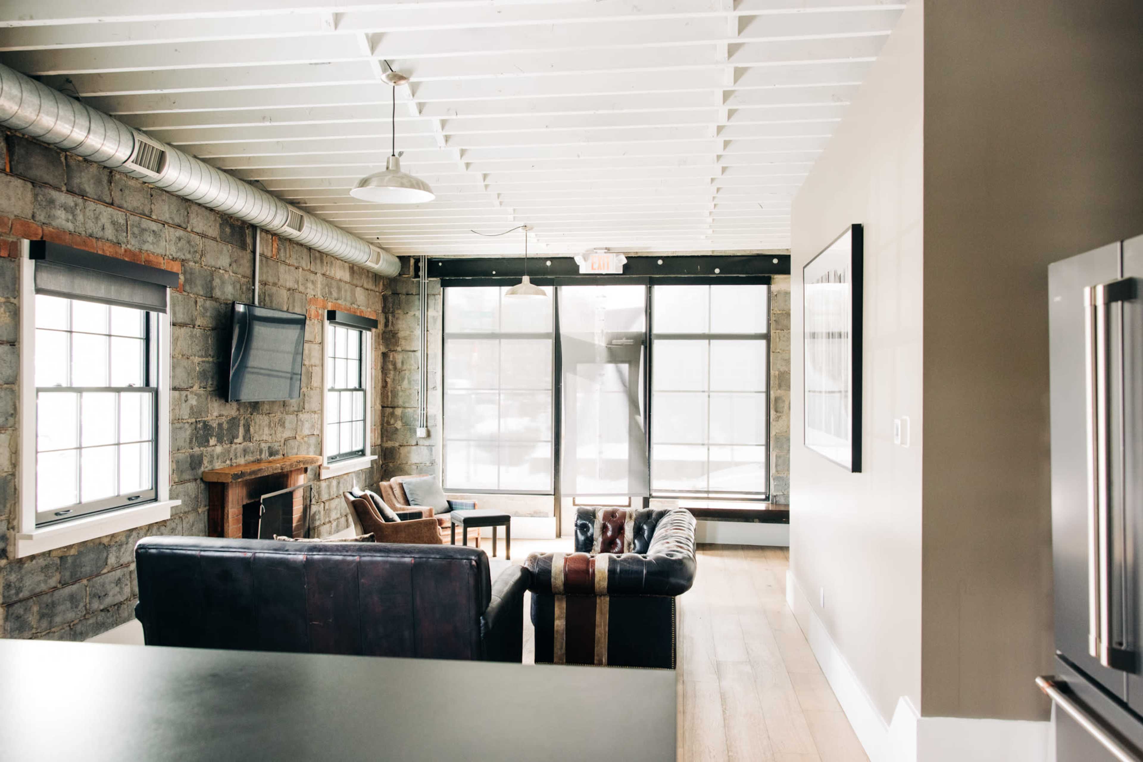 The image shows a modern living room featuring stone walls, large windows, and a mix of leather and wooden furniture.